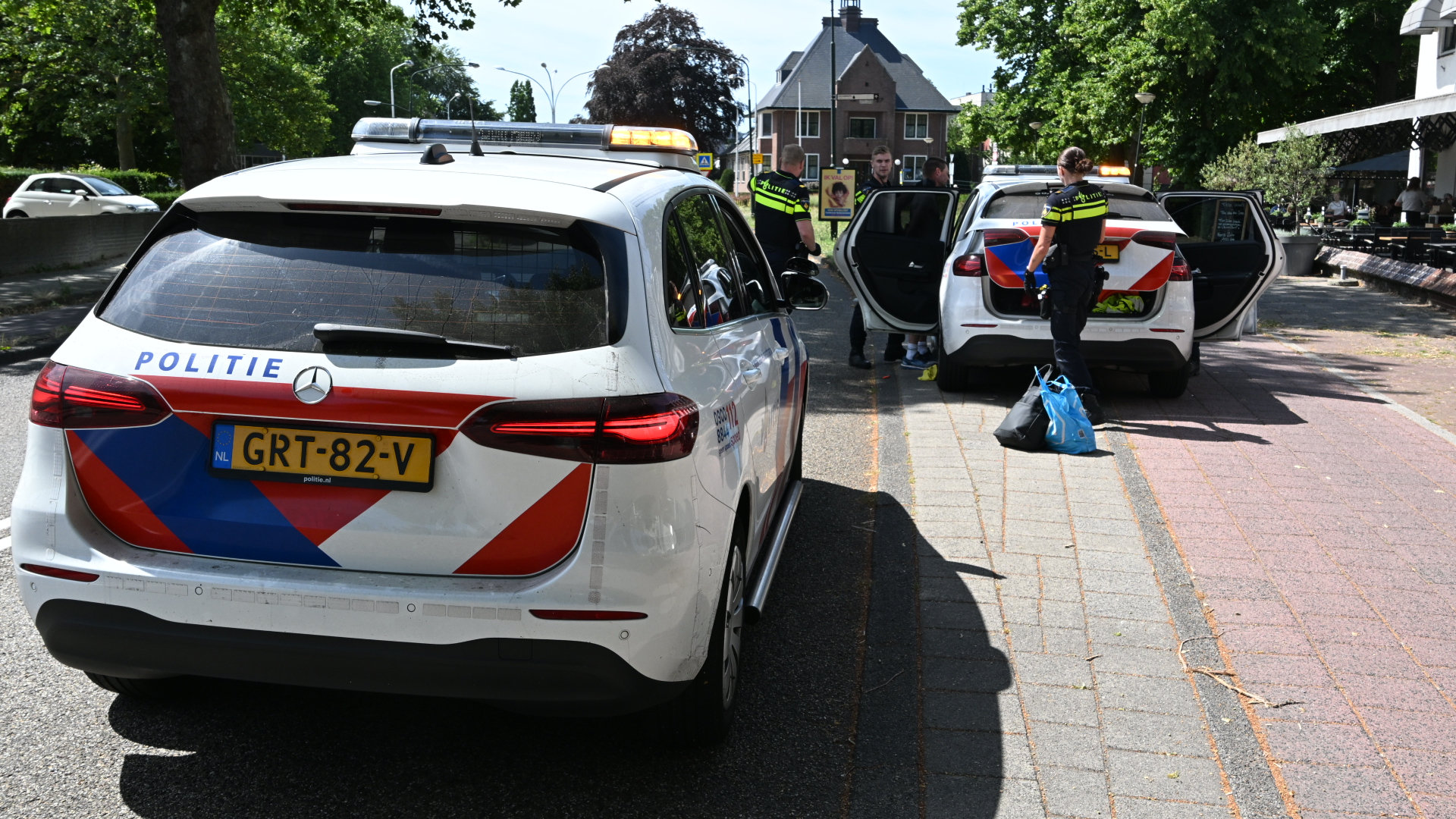 Twee Nederlandse politieauto’s met zwaailichten langs de weg, agenten staan bij open achterdeuren tijdens een controle