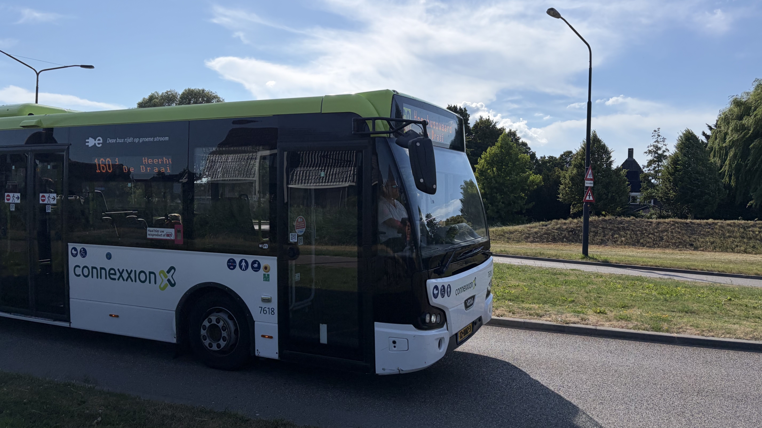 Connexxion-stadsbus met groene dakrand op de weg, lijn 160 richting Meerhoven De Dries, bij groenstrook