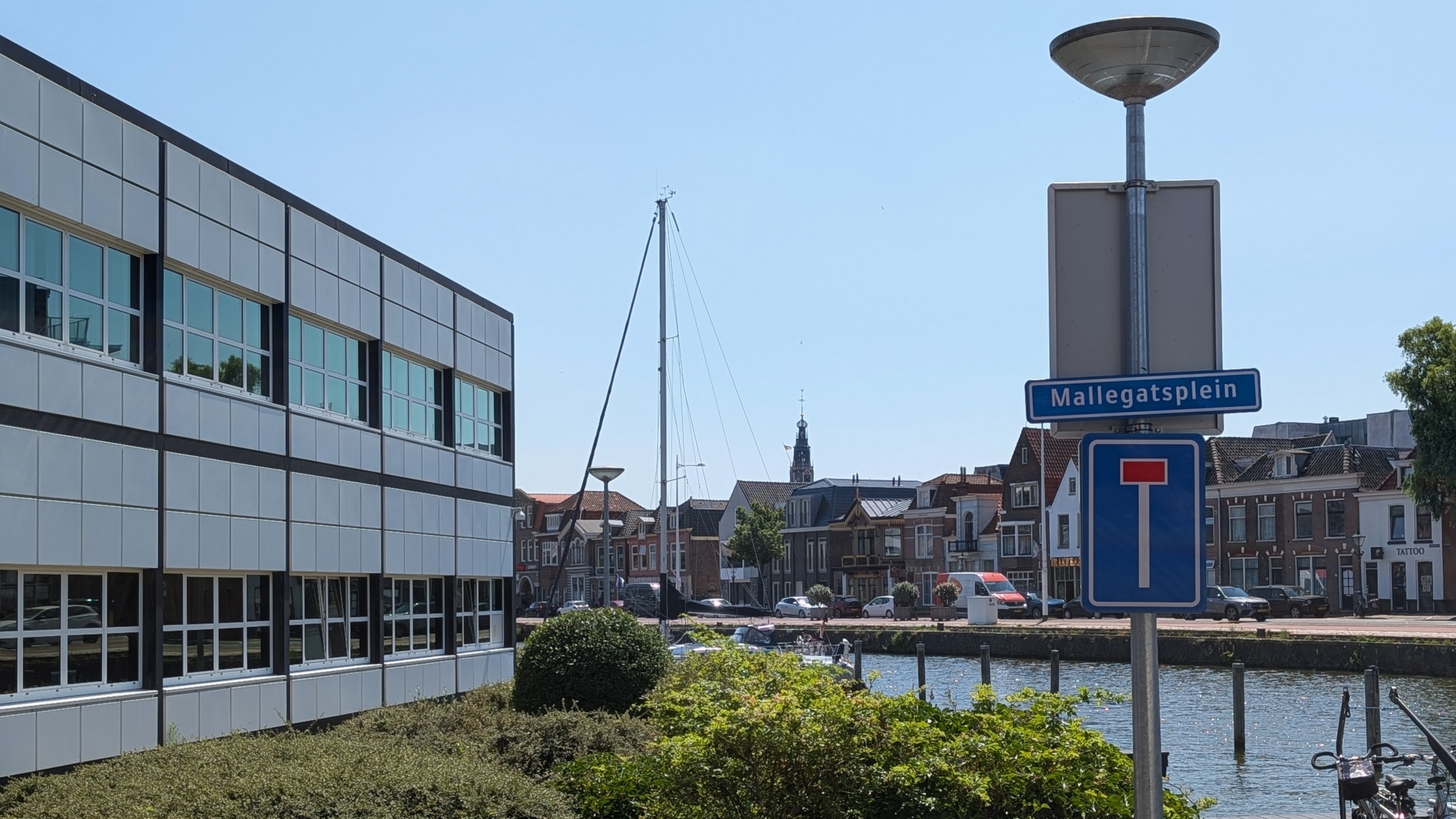 Straatbord Mallegatsplein met doodlopend-weg-teken, met kanaal, boten en gevels op de achtergrond