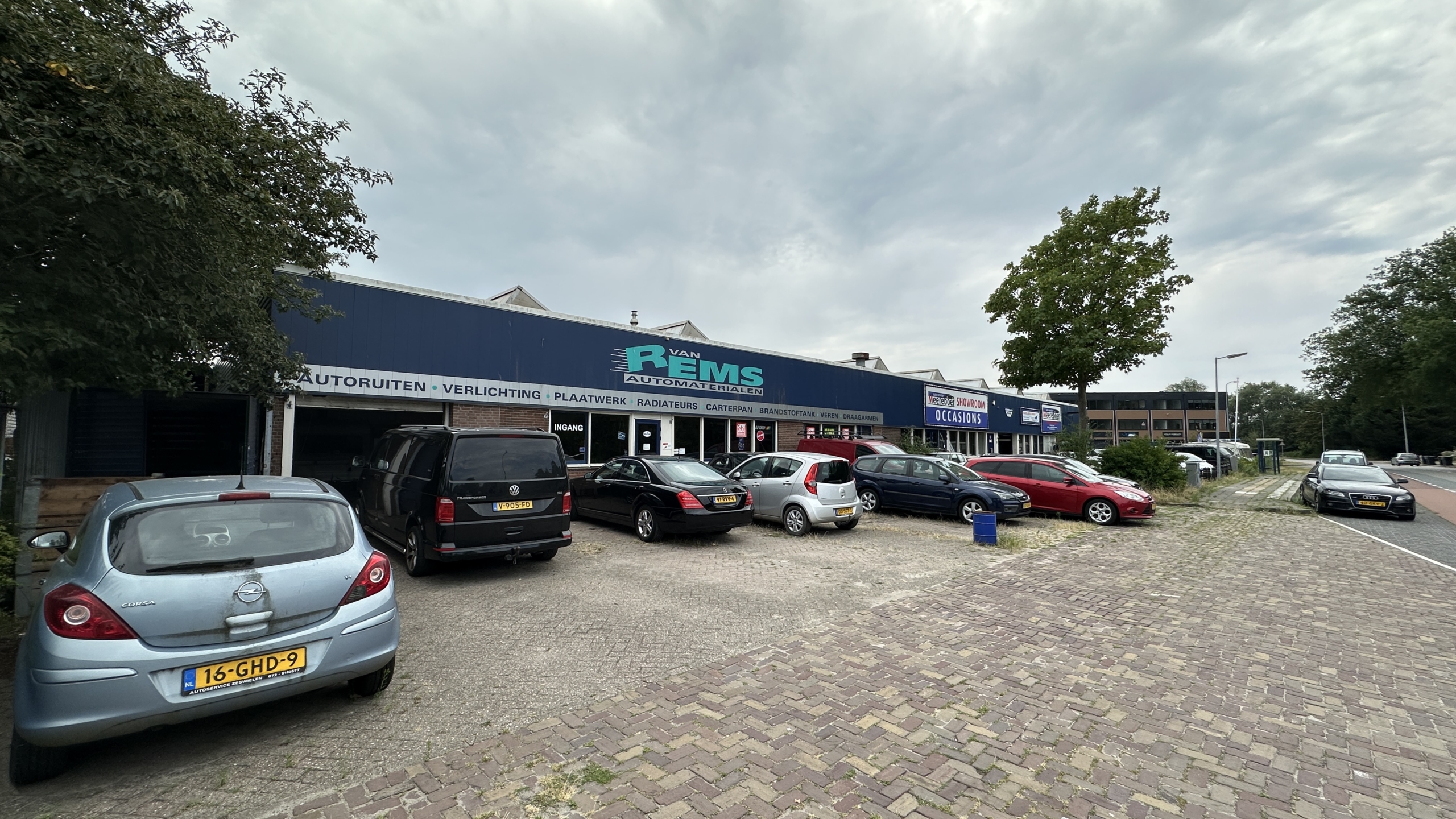 Parkeerterrein met auto’s voor het pand van Van Rems automaterialen, met bord ‘Occasions’ en ‘Showroom’