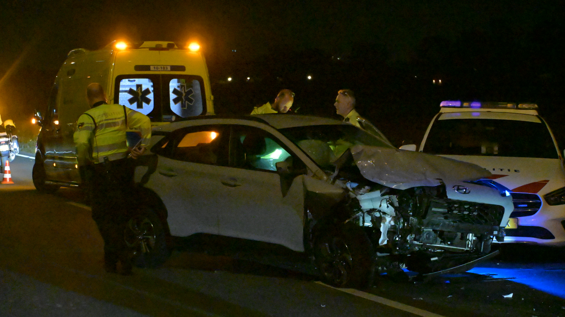 Nachtelijk verkeersongeval met zwaar beschadigde auto, politieagenten, ambulance en politiewagen met zwaailicht