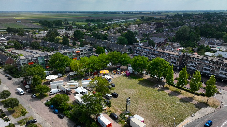 Luchtfoto van woonwijk met grasveld waar een kleine kermis en enkele witte tenten en busjes staan