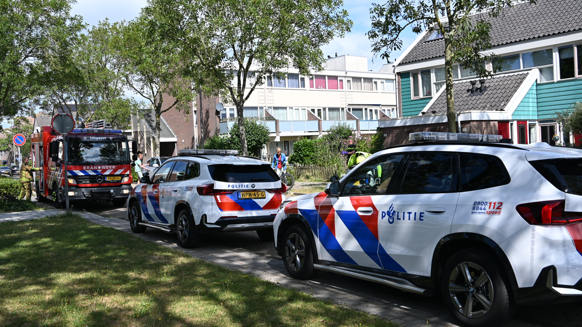 Brandweerwagen en twee politieauto’s staan langs een woonstraat met hulpverleners bij de voertuigen