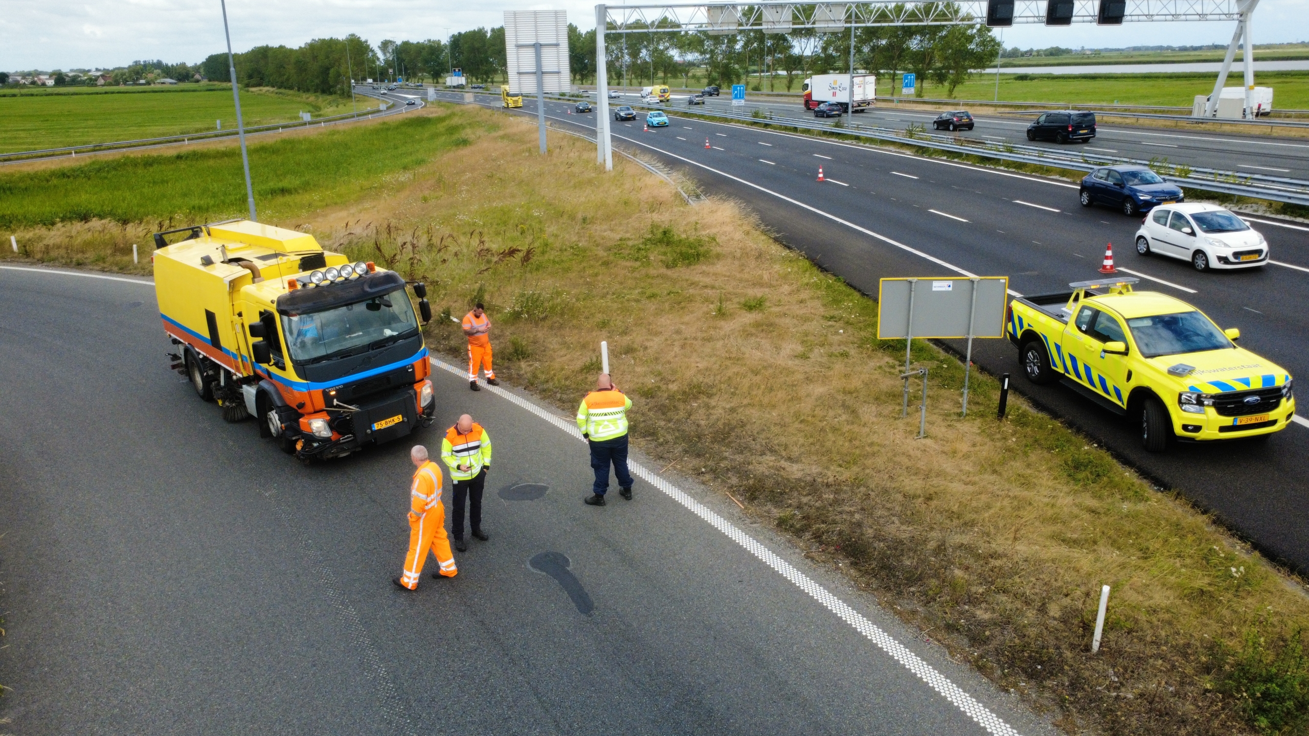 Weginspecteurs en wegwerkers bij een gele markeerwagen en servicepickup langs de snelweg met afgezette rijstrook