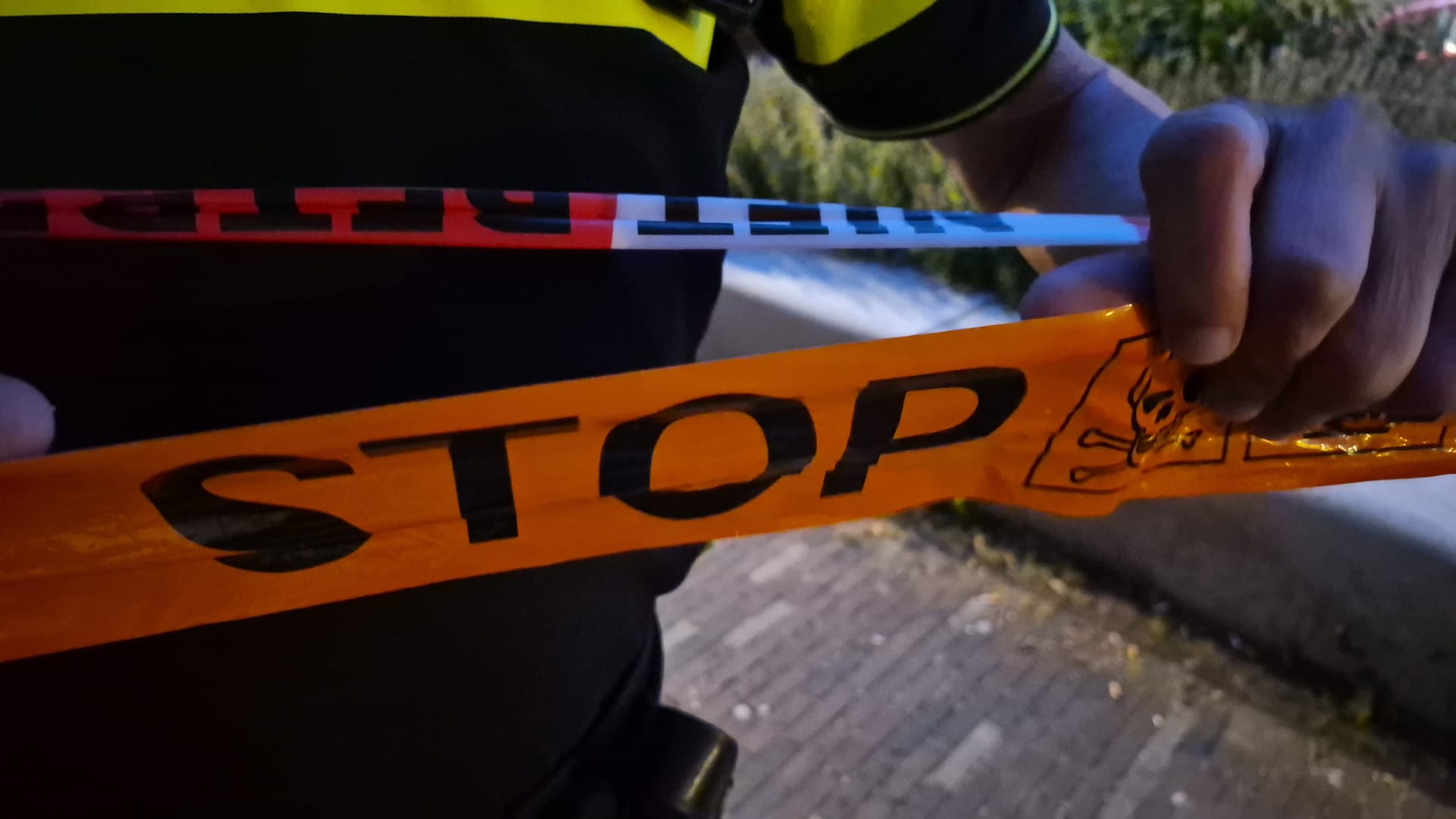 Handen die politielint en oranje STOP-lint met doodskopsymbool vasthouden bij een afgezet gebied buiten