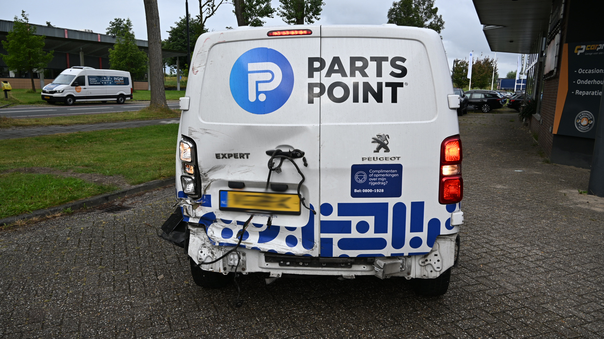 Achterkant van PartsPoint-bestelbus met schade linksachter en loshangende bedrading, geparkeerd op straat