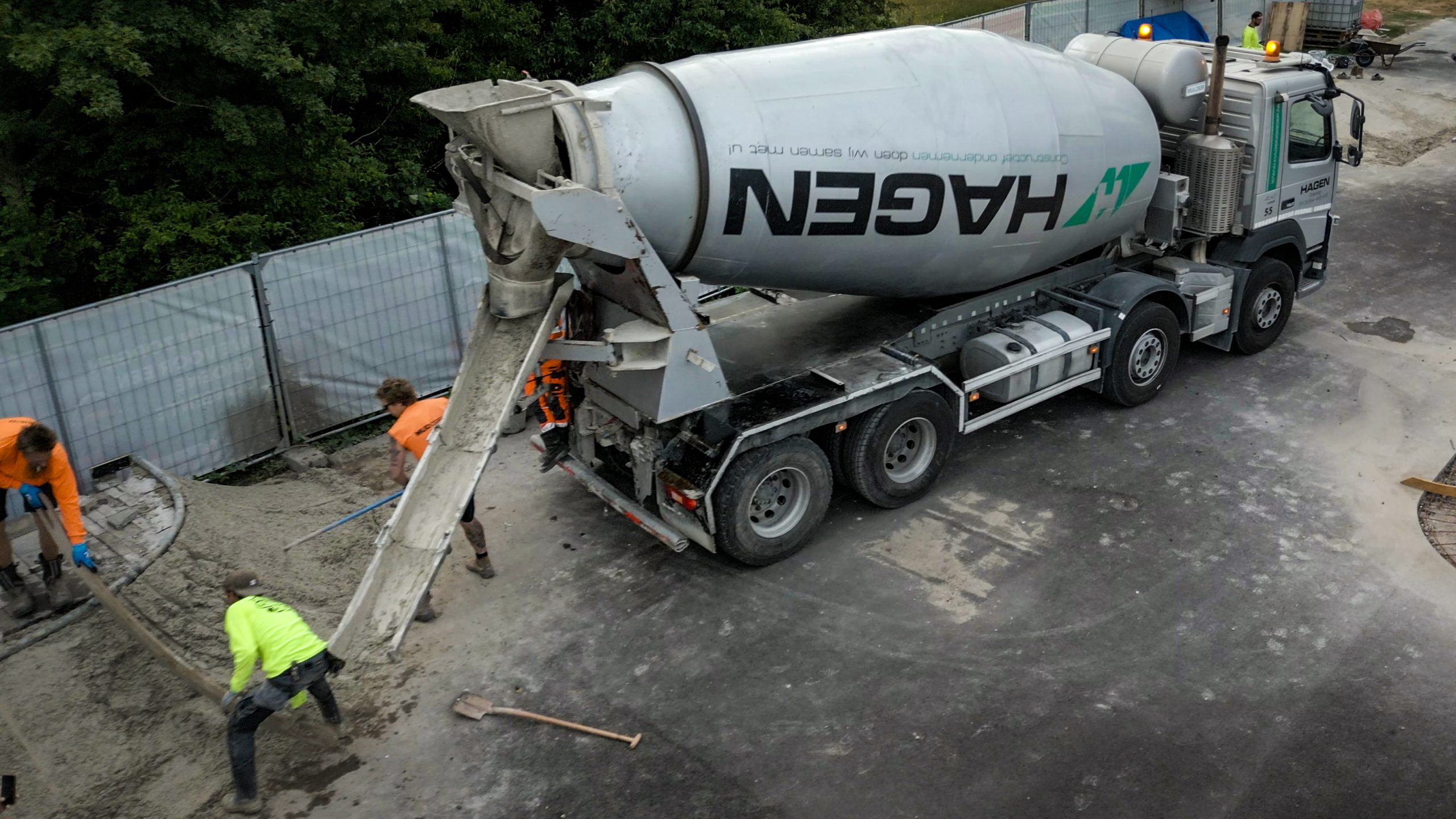 Betonmixertruck stort beton via een glijgoot terwijl bouwvakkers het beton verdelen op een bouwplaats