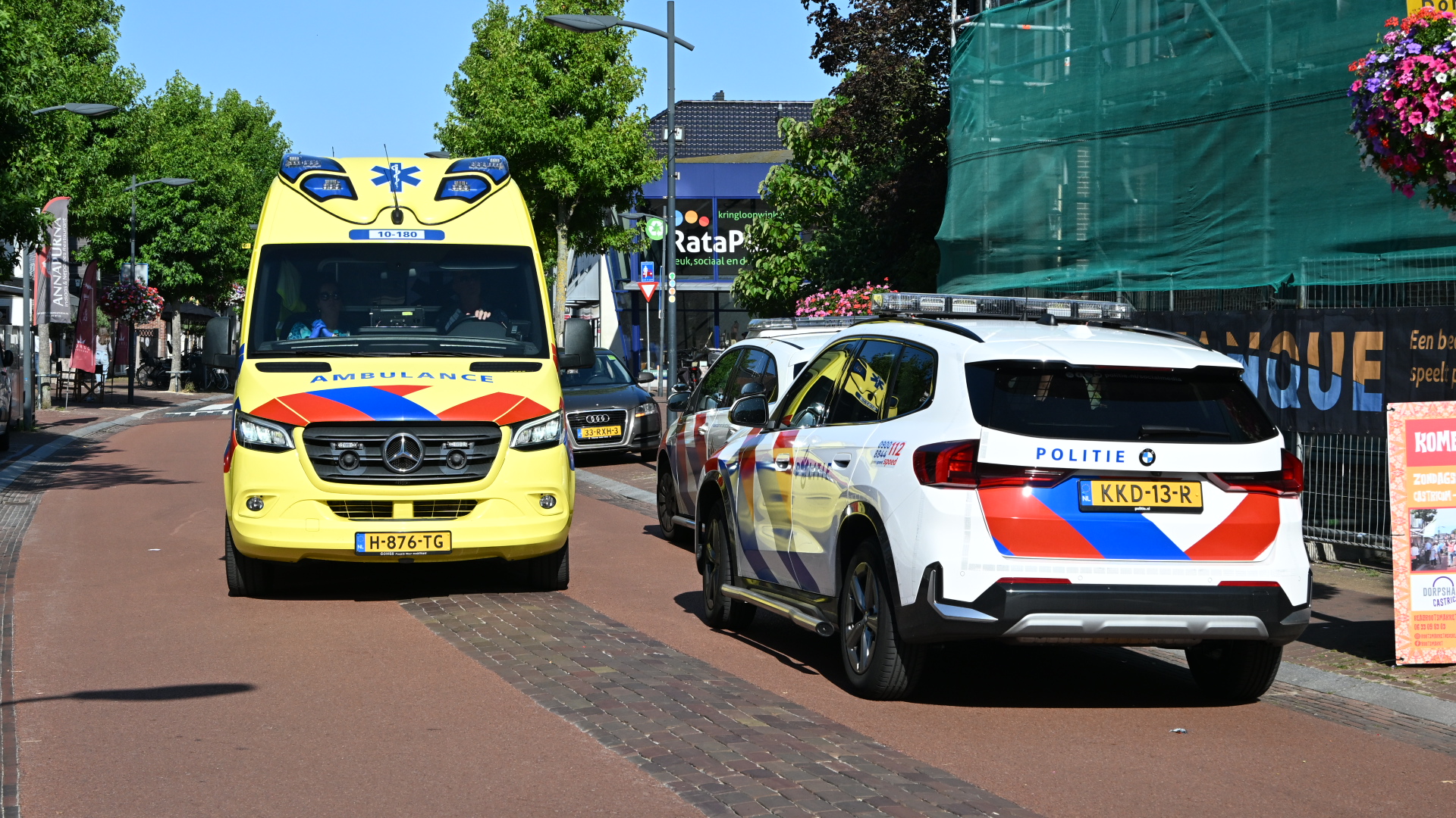 Ambulance en politieauto op een dorpsstraat, met de ambulance frontaal in beeld en de politieauto ernaast geparkeerd