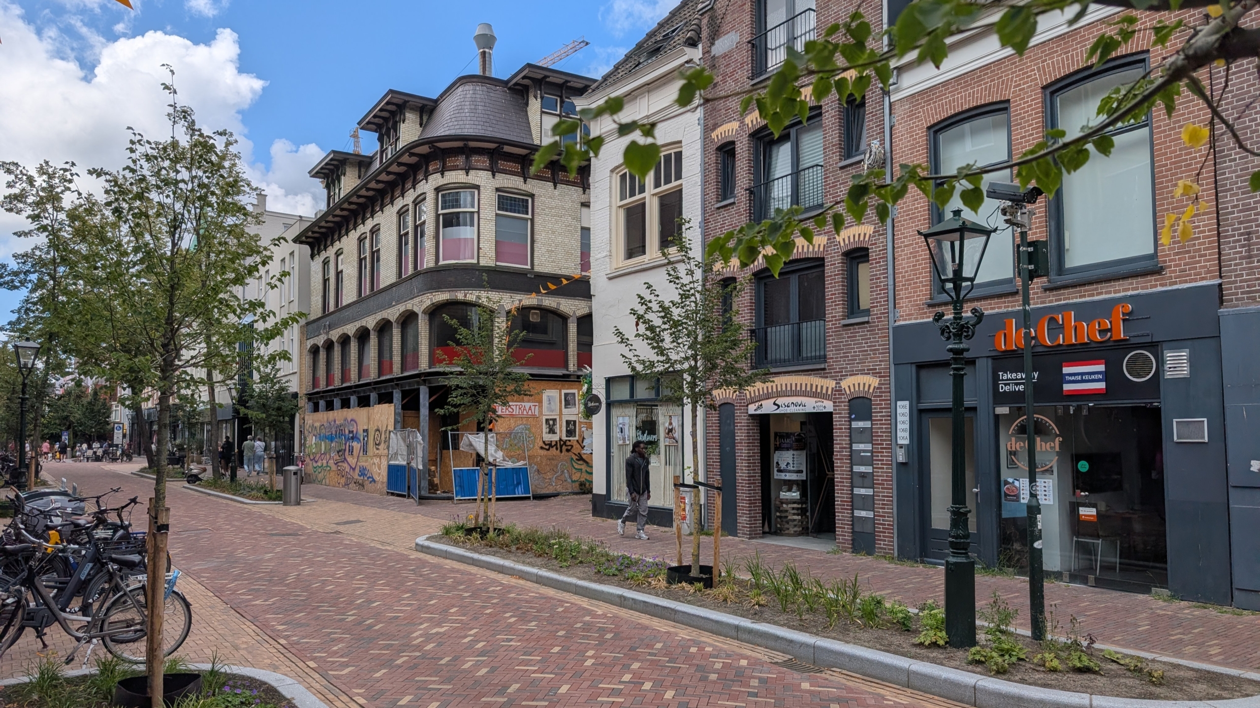 Stadsstraat met bakstenen panden, fietsen en een winkelpui “de Chef”, naast een deels afgezet en beklad gebouw