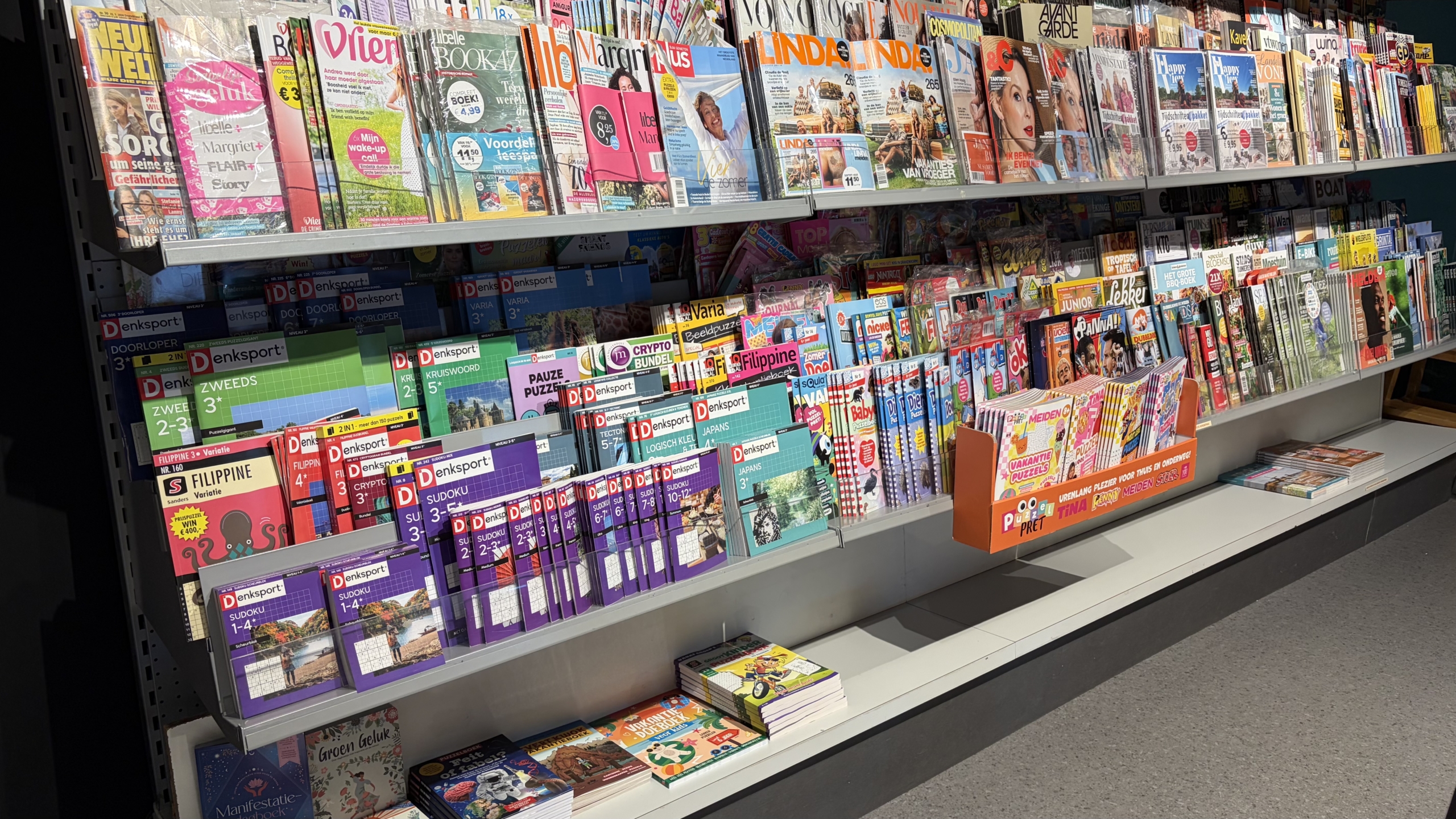 Tijdschriftenrek in een winkel met glossy magazines, puzzelboekjes en kinderbladen op meerdere schappen