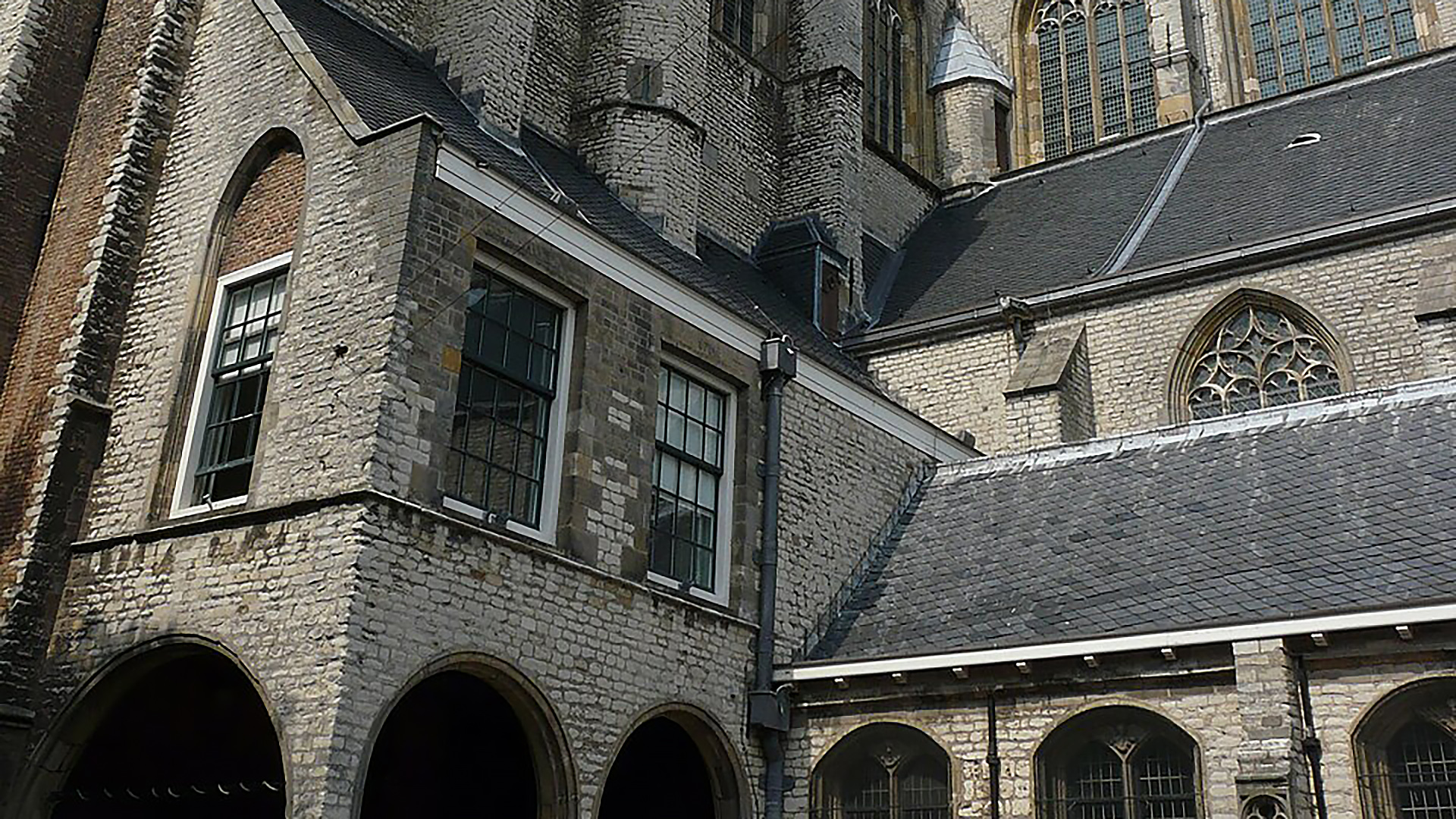 Middeleeuws stenen gebouw met hoge ramen, gotische boogvensters en een dakbedekking van donkere leisteen.