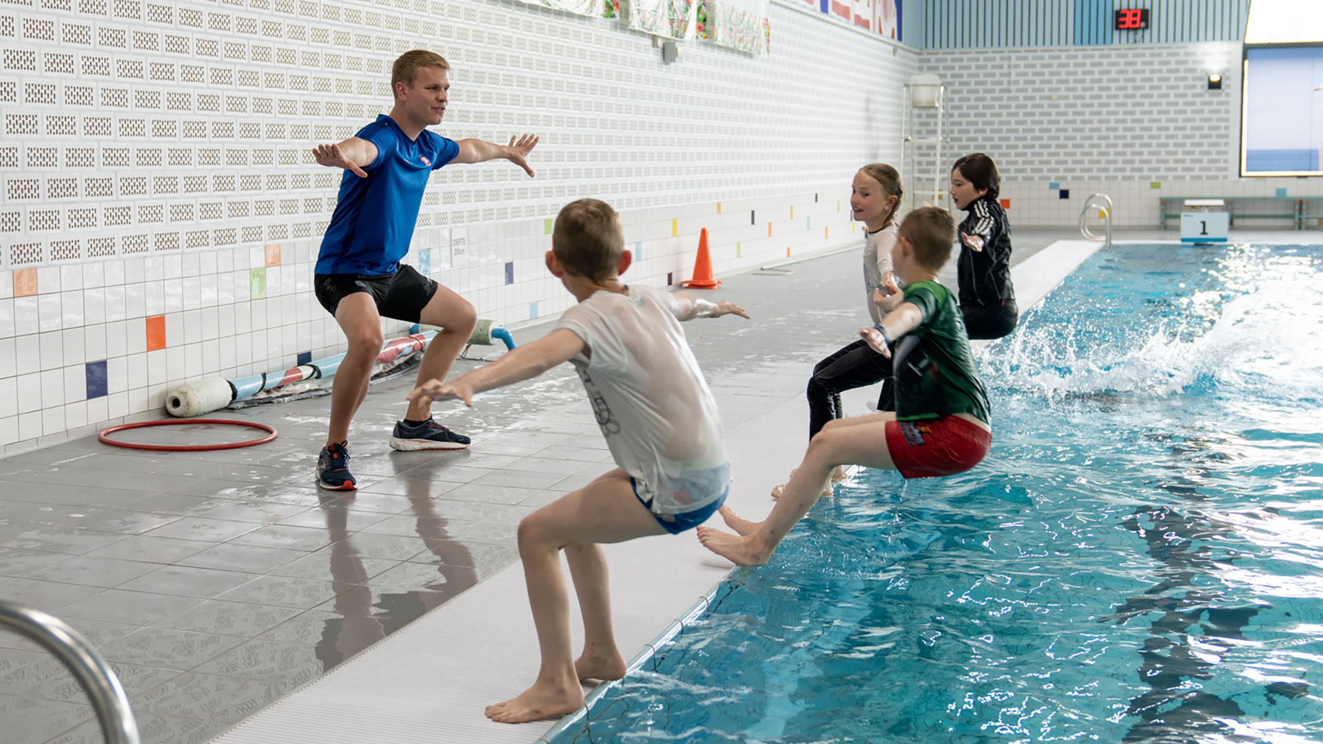 Een instructeur geeft zwemoefeningen aan kinderen die vlakbij het zwembad staan in sportkleding.