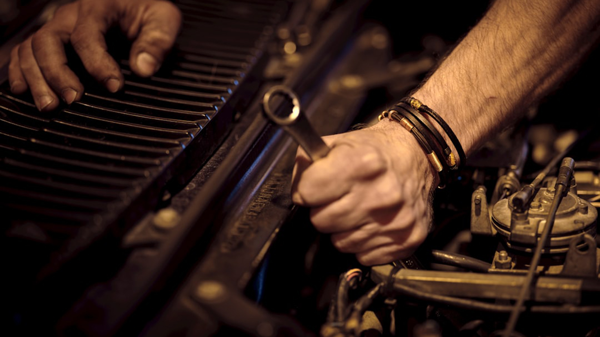 Close-up van handen die met een steeksleutel aan een automotor sleutelen, naast het radiatorrooster
