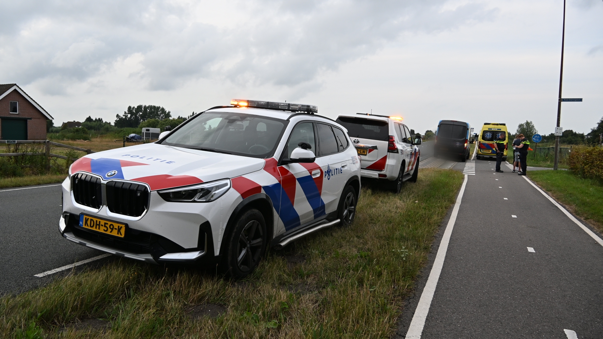 Nederlandse politieauto’s en ambulance met zwaailichten langs de weg, agenten bij een incident op het fietspad