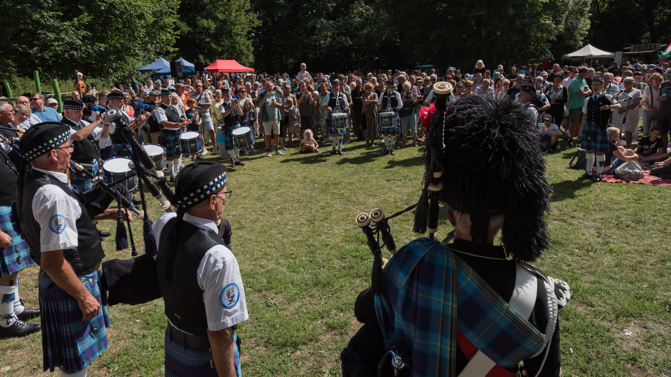 Doedelzakband in kilt speelt op grasveld, omringd door groot publiek bij een openluchtfestival