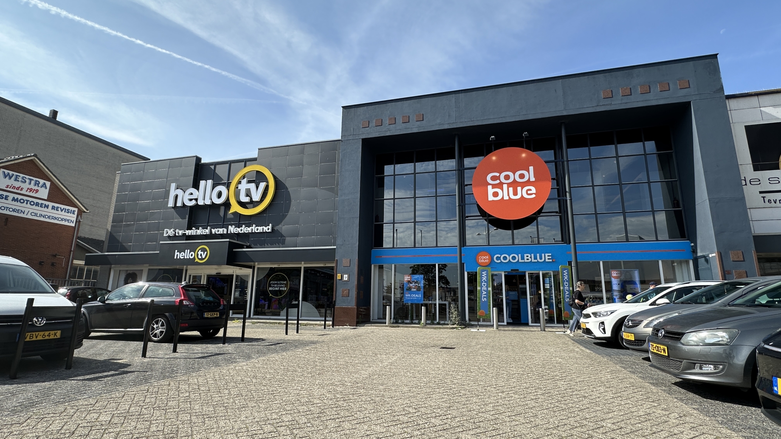 Gevel van winkels HelloTV en Coolblue met groot Coolblue-logo, seen vanaf parkeerplaats met geparkeerde auto’s