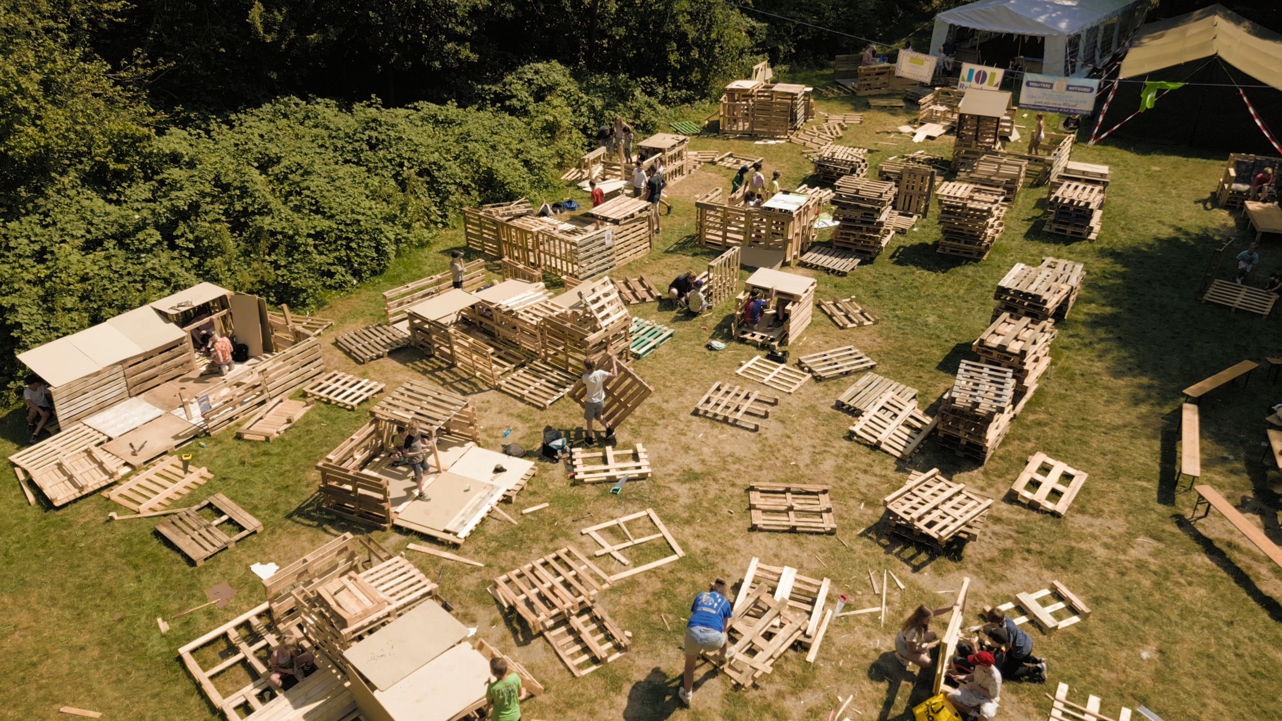 Luchtfoto van mensen die op een grasveld met houten pallets tijdelijke hutten en constructies bouwen