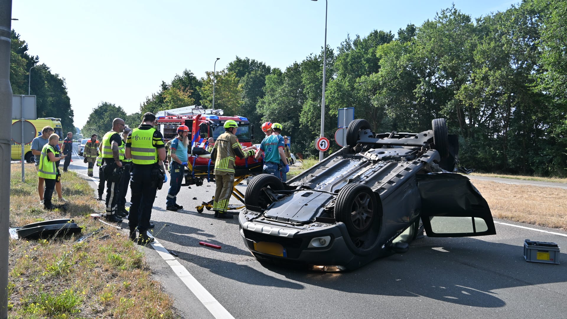 Hulpdiensten en politie bij een ongeval op de weg, met een auto die op zijn dak ligt en een brancard ernaast