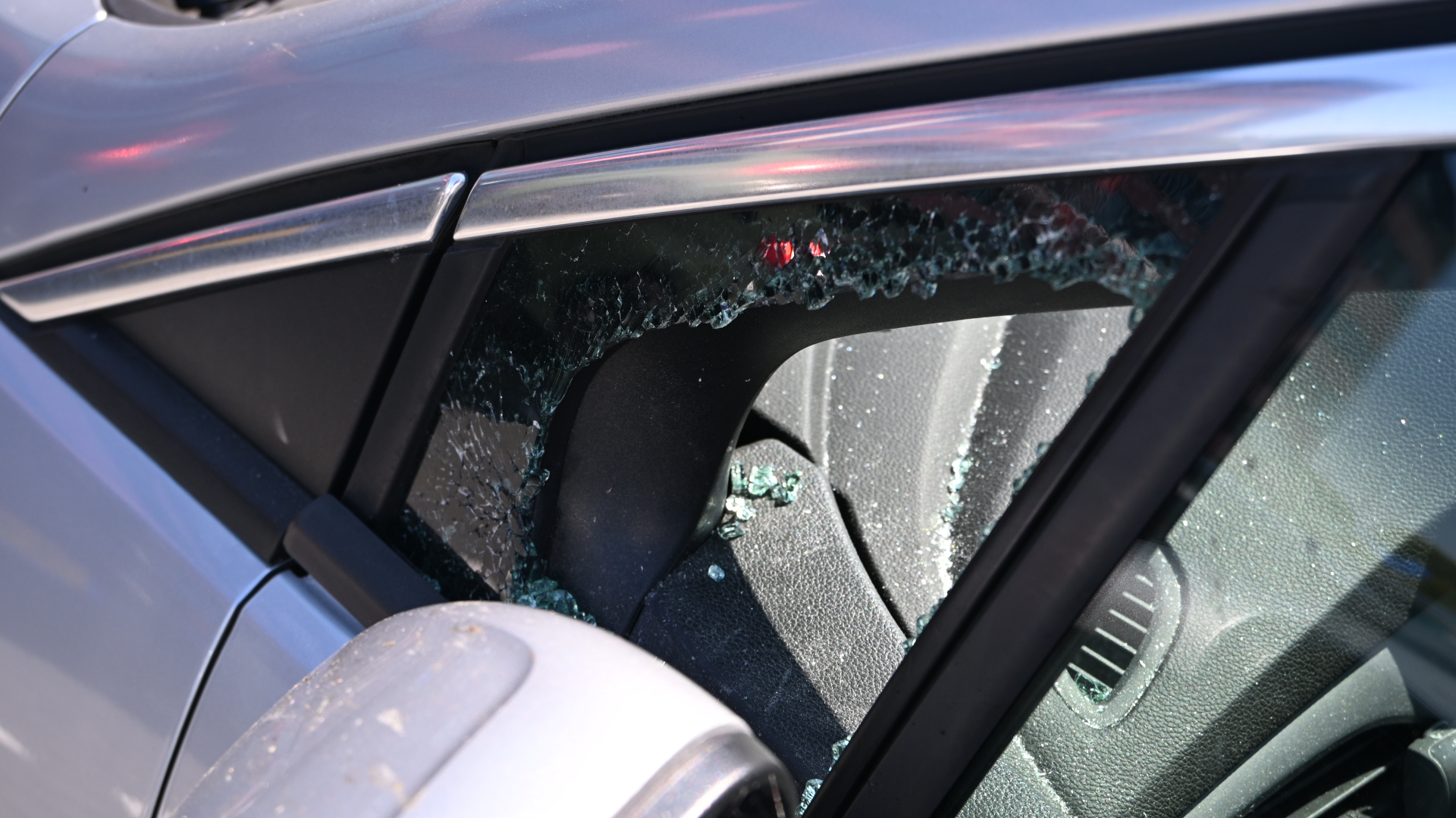 Kapotte zijruit van een auto met gebroken glas in het portier en zichtbare veiligheidsgordel binnenin