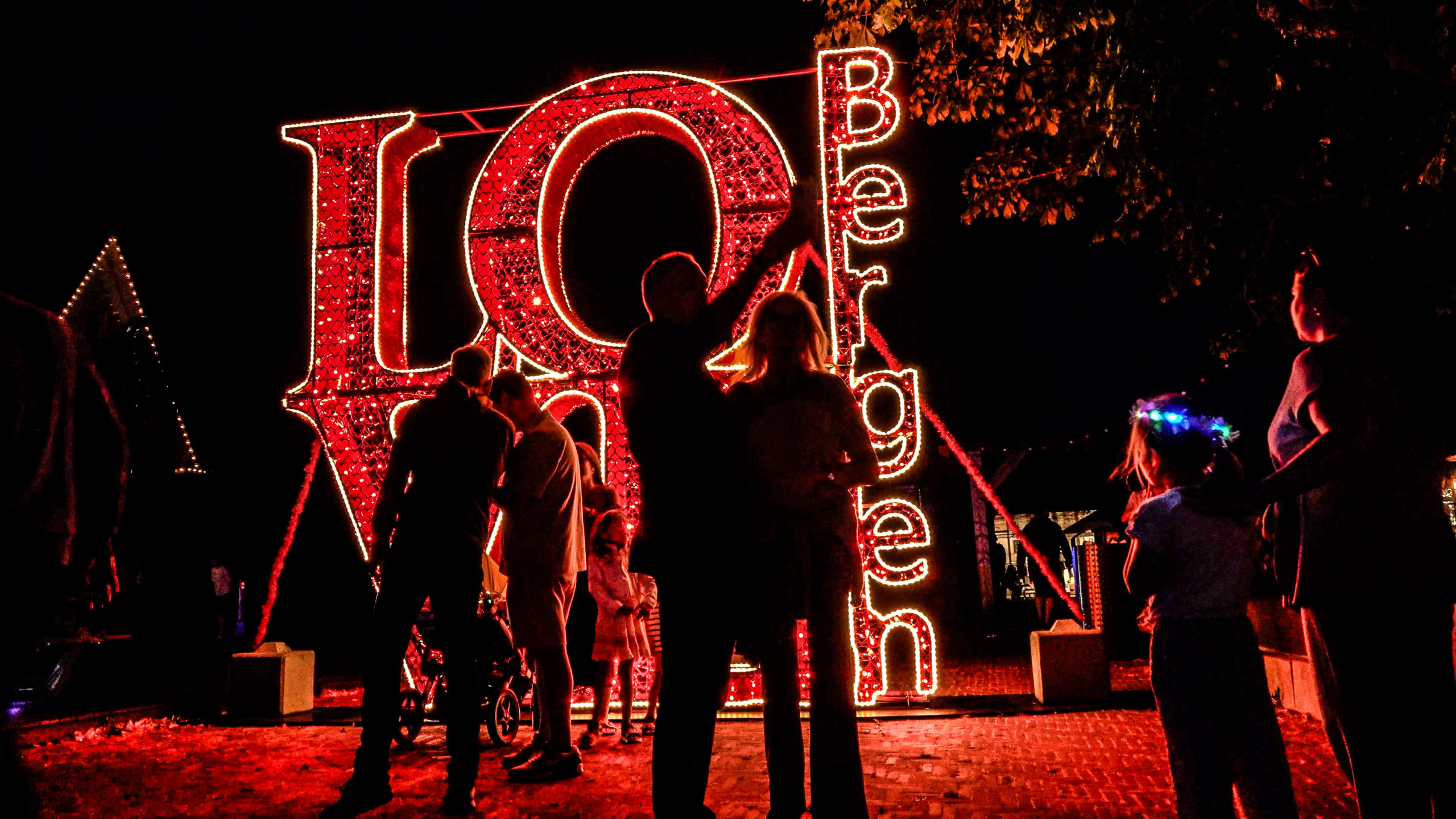 Silhouetten van bezoekers voor een fel verlichte rode installatie met de letters I Q en het woord Performing verticaal
