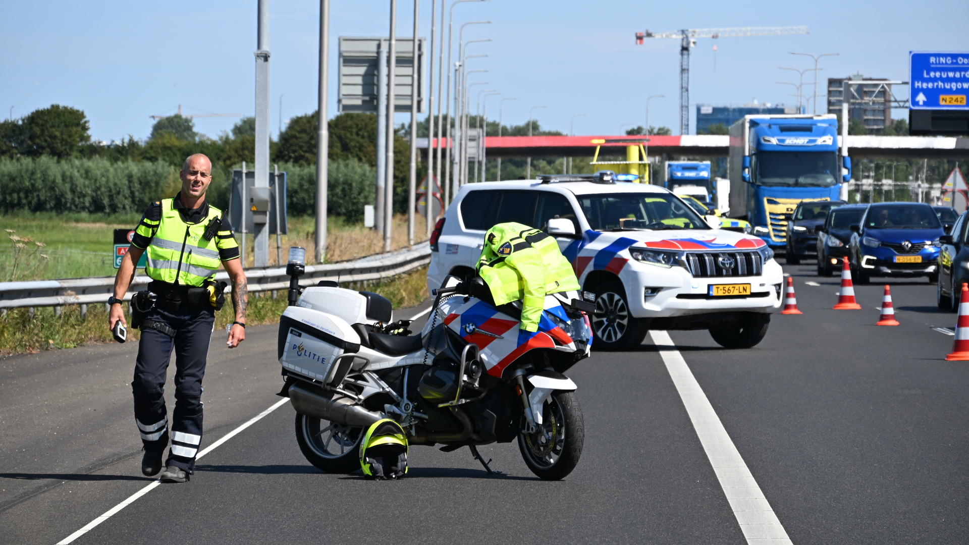 Politieagenten en motor op de snelweg bij een met pionnen afgezet incident, met politieauto en file op de achtergrond