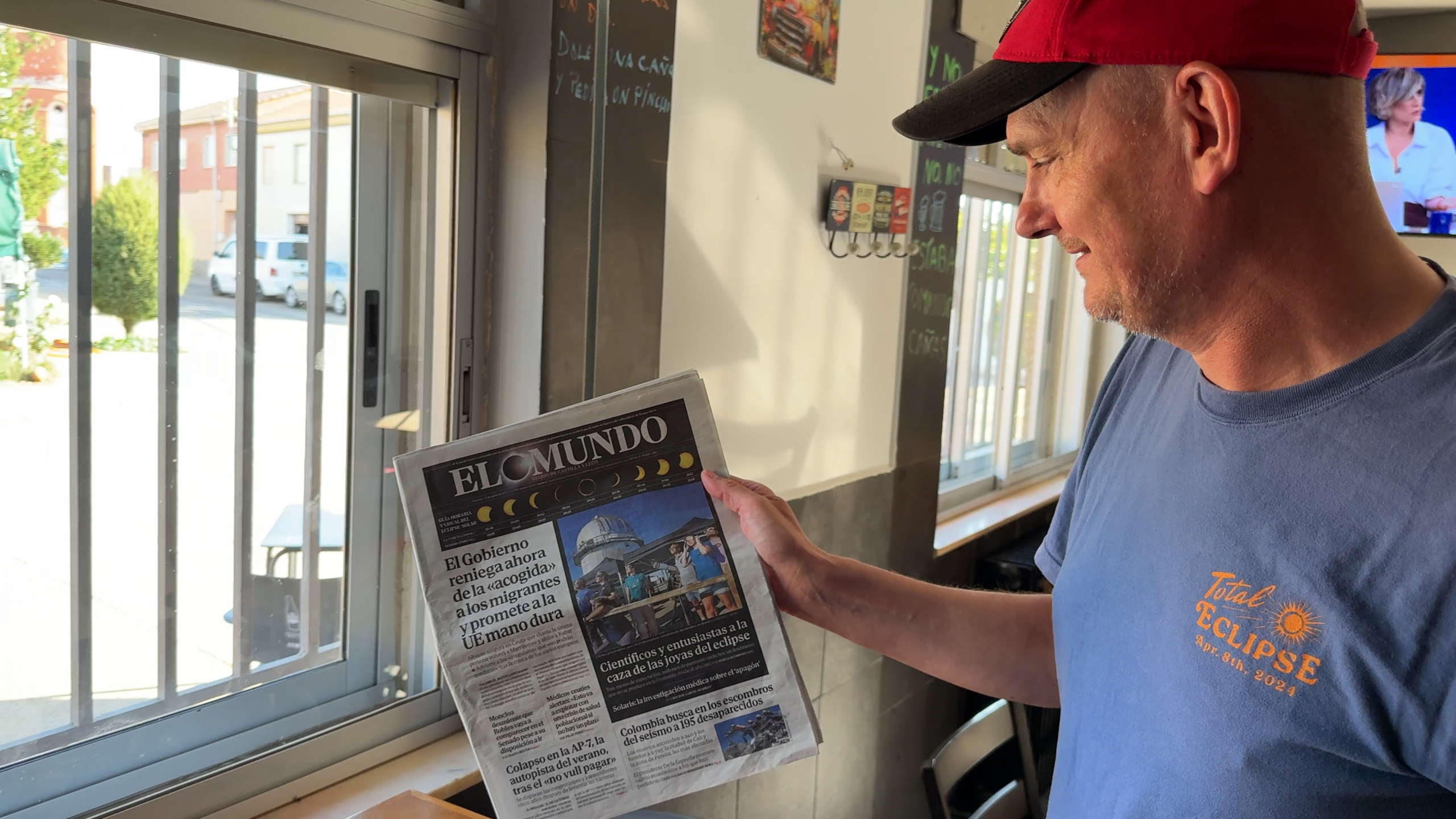 Man met rode pet leest krant El Mundo in een café bij het raam