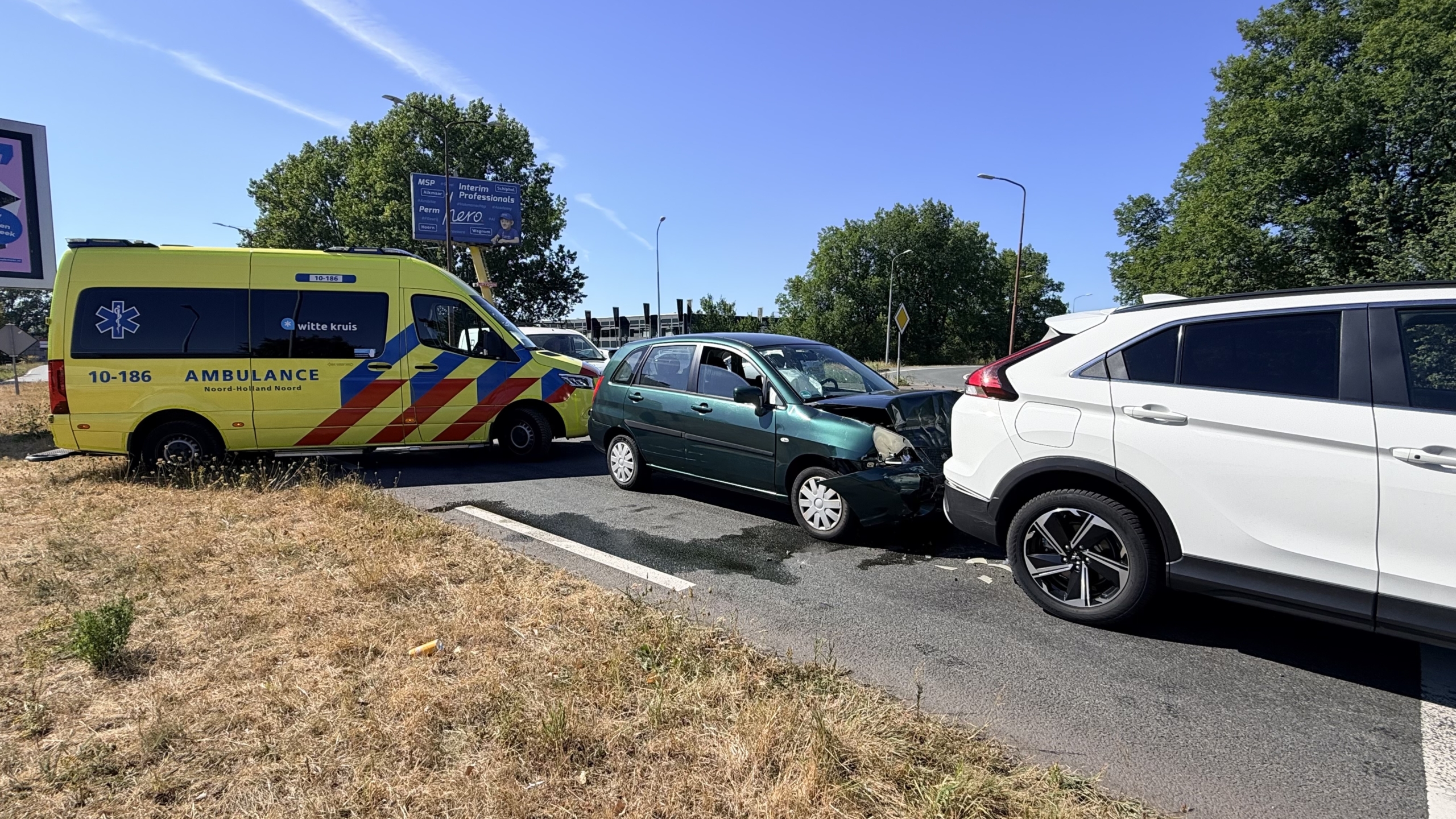 Ambulance naast botsing waarbij een groene auto achterop een witte SUV is gereden op een kruising