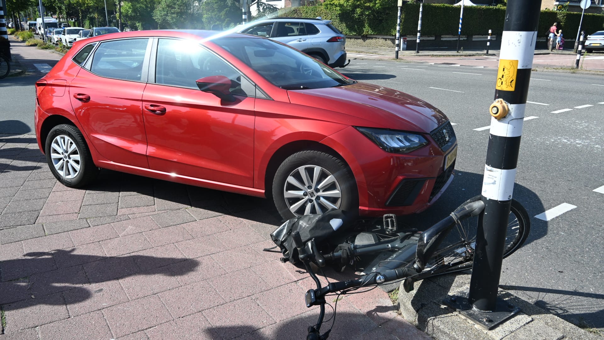 Rode auto op de stoep bij een kruispunt; een omgevallen fiets ligt tegen een paal met oversteekknop