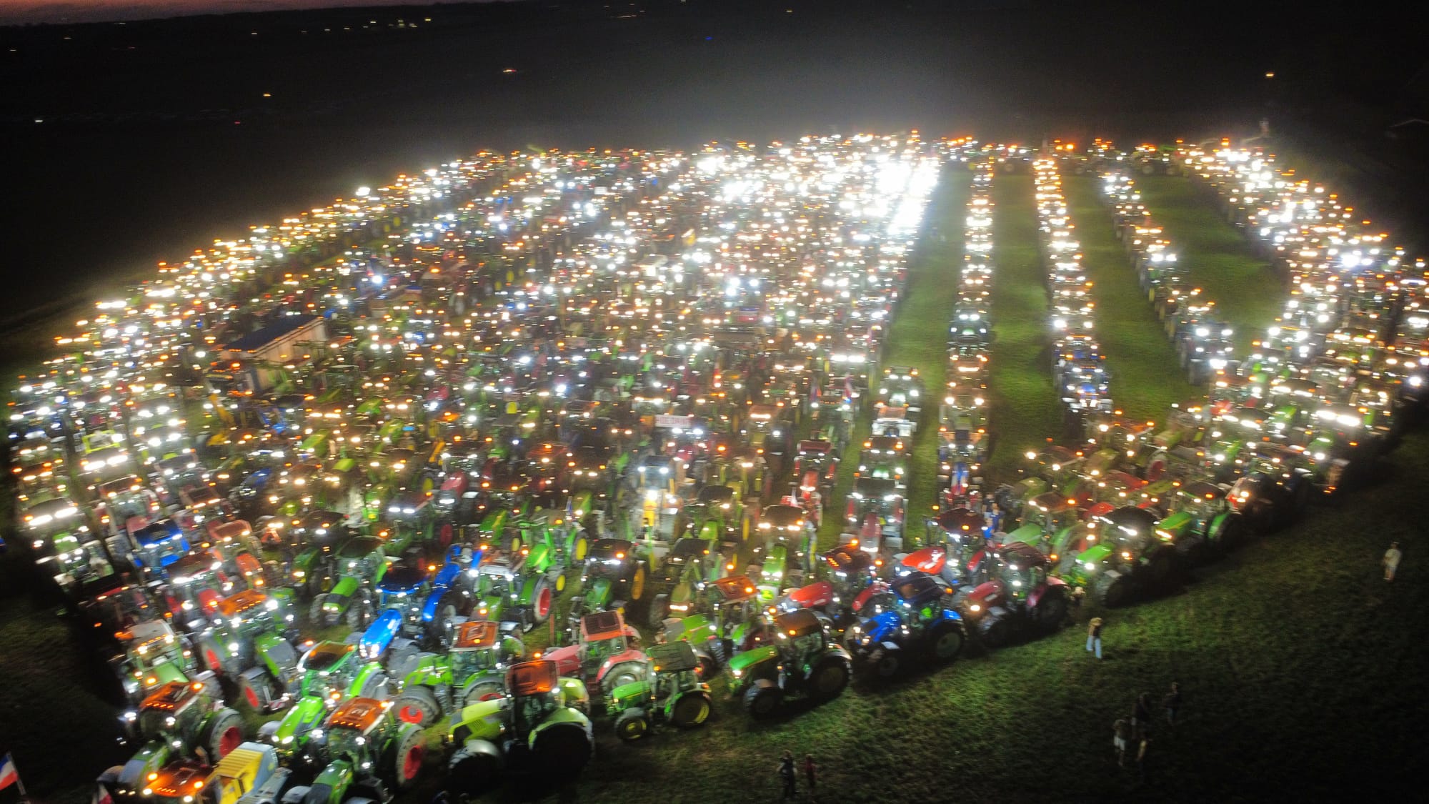 Luchtfoto bij nacht van honderden tractoren met brandende lichten, opgesteld in rijen op een veld