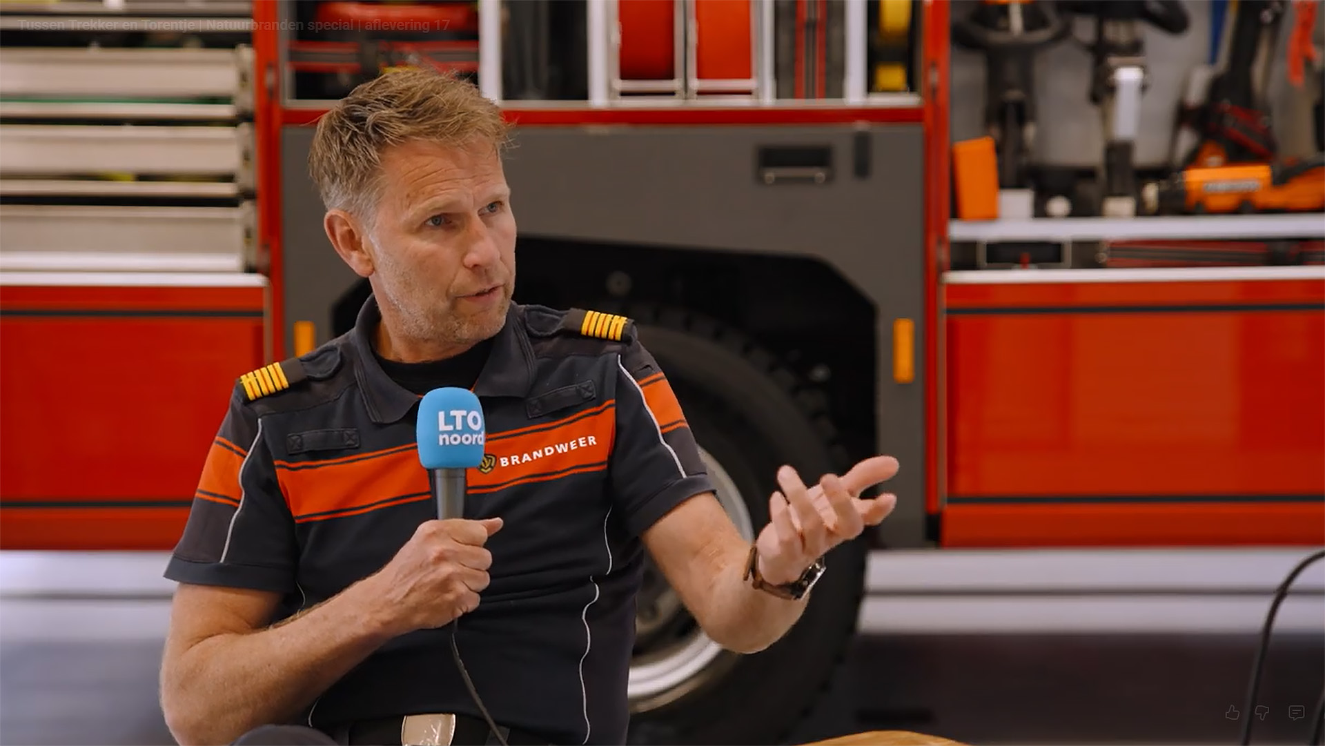 Brandweerman in uniform geeft interview met LTO Noord-microfoon, met brandweerwagen op de achtergrond