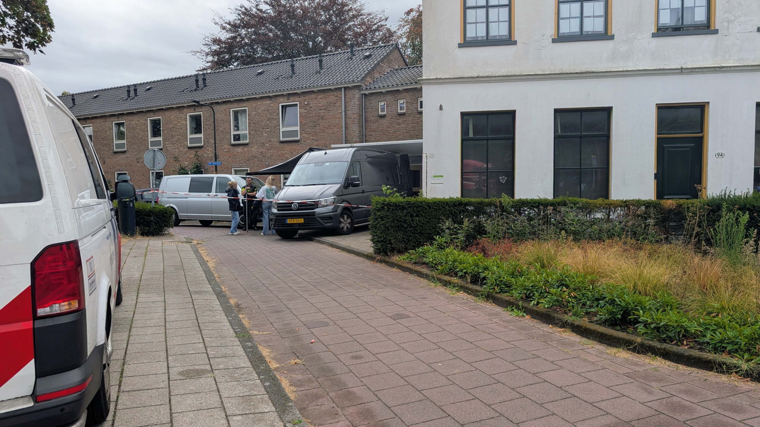 Afgezette straat met twee bestelbusjes en enkele mensen bij een gebouw met grote ramen en voordeur nummer 94