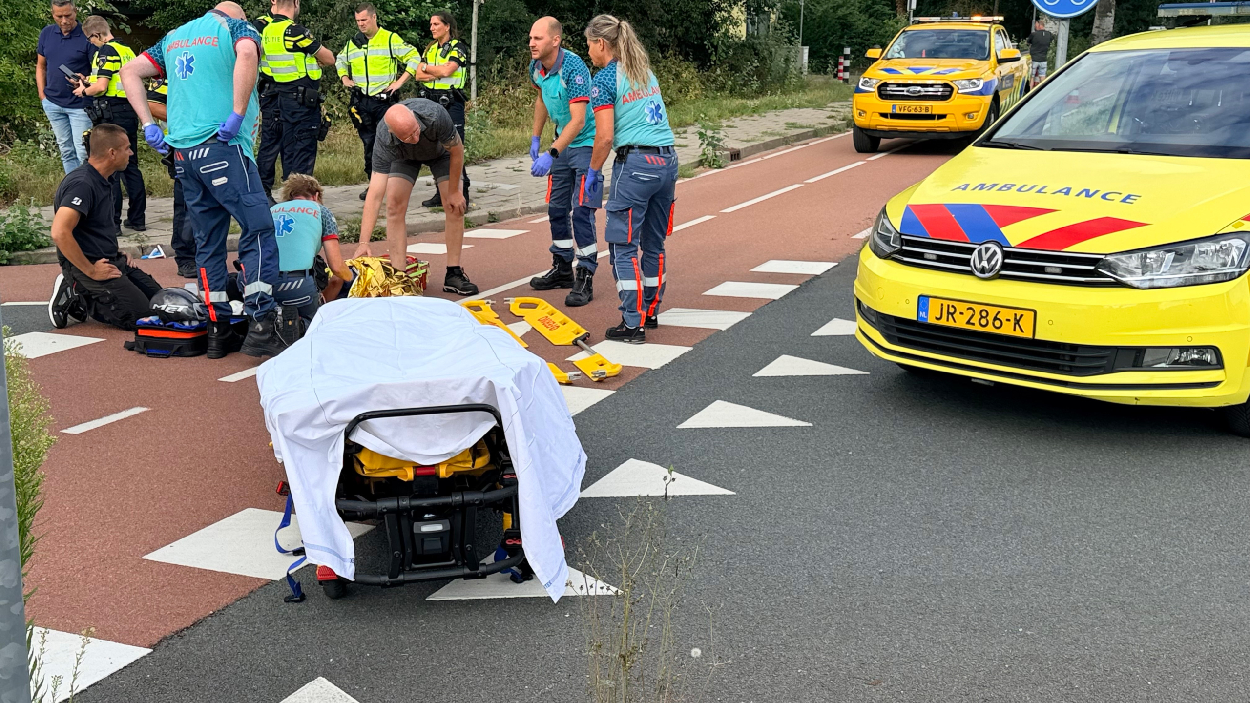 Hulpverleners en politie verlenen eerste hulp op de weg naast een ambulance en brancard met laken