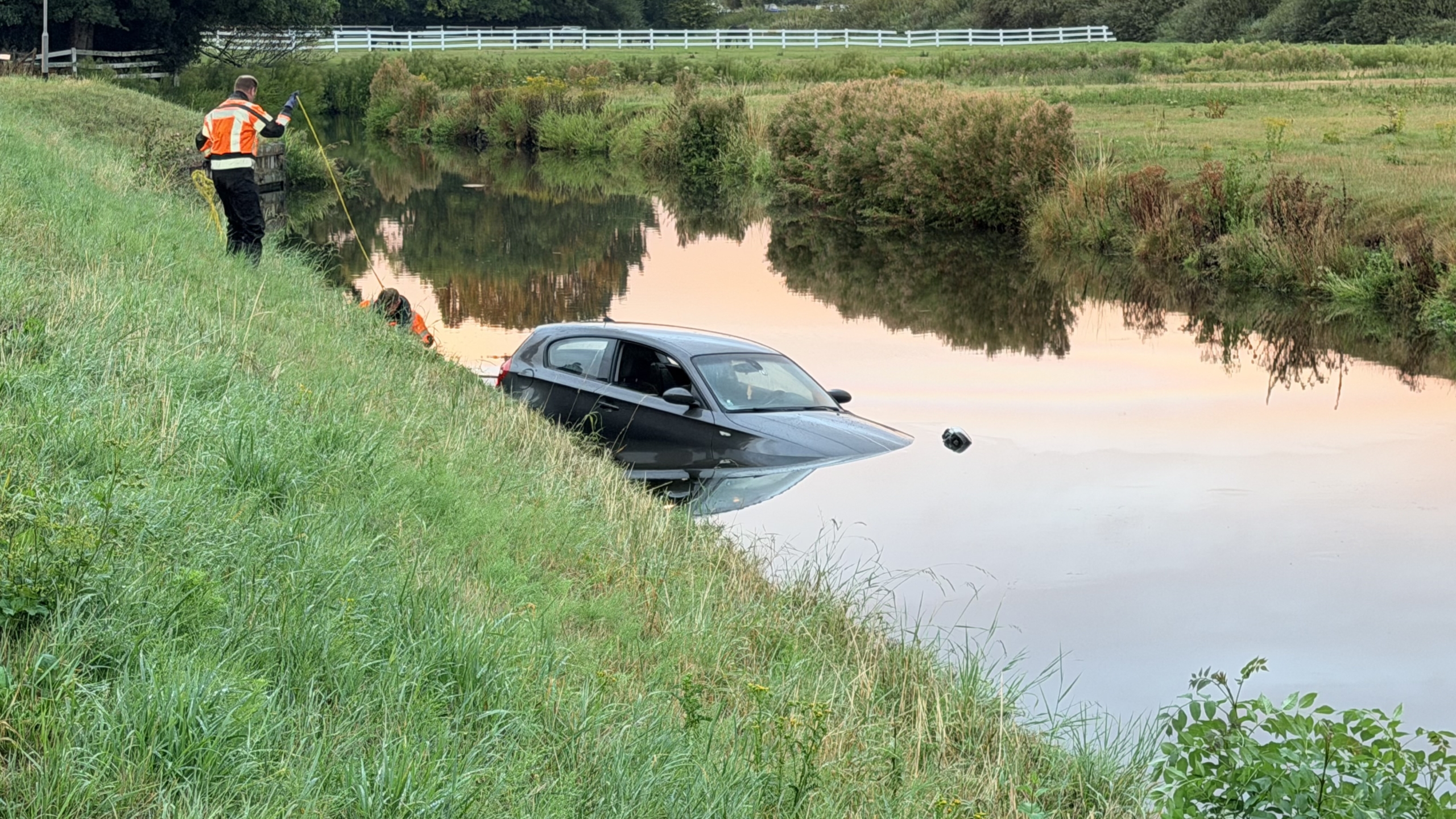 Hulpdiensten in fluorescerende jassen bergen een half ondergelopen auto uit een sloot langs een grasdijk