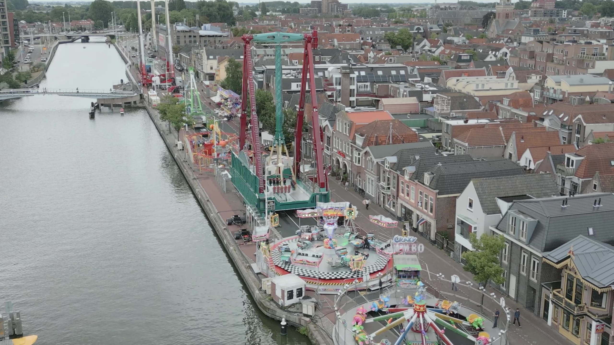 Luchtfoto van een kermis langs een kanaal met draaimolen en hoge attracties tussen huizen en bruggen