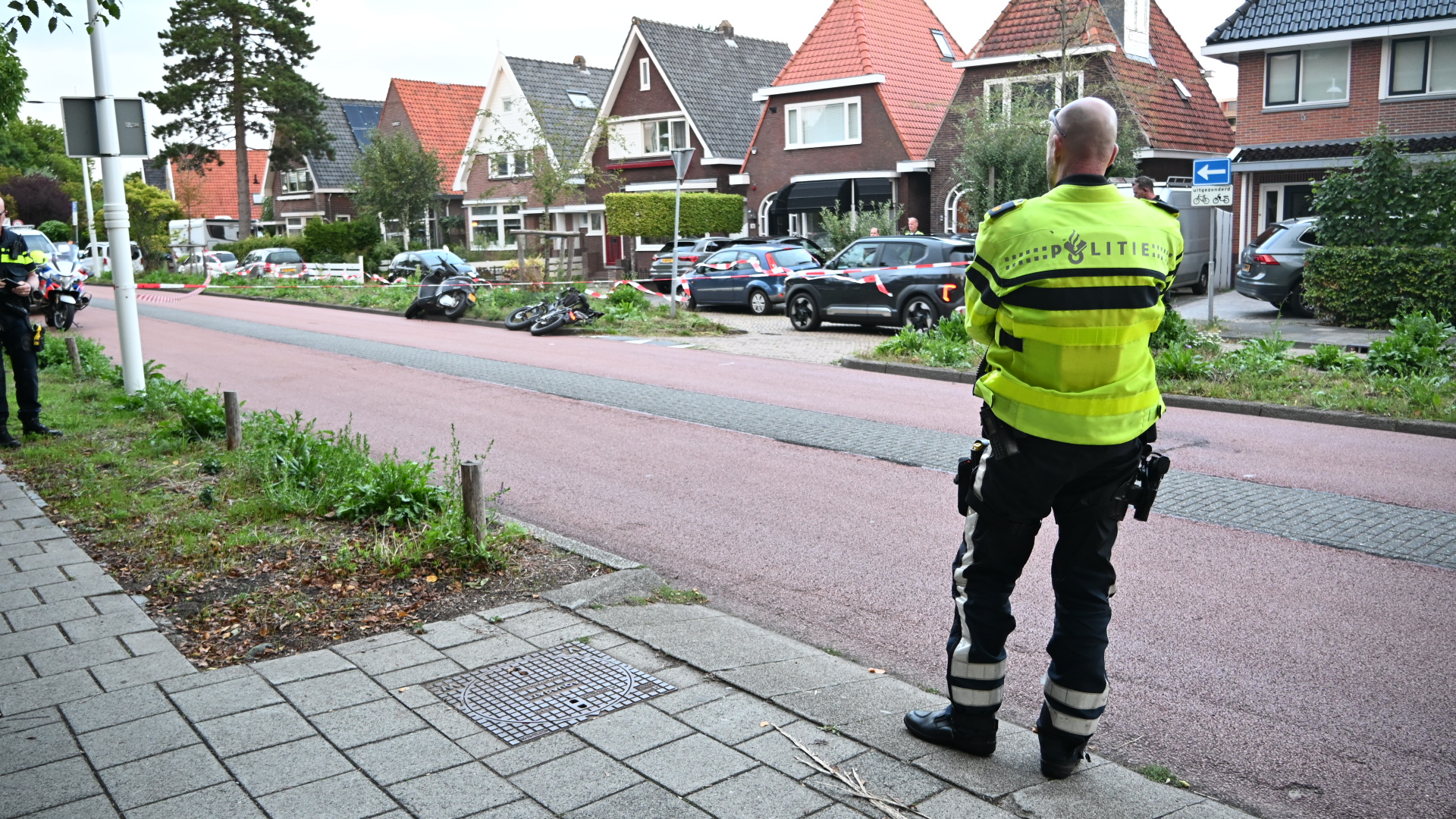 Politieagent bij afgezet ongeval op woonstraat, met omgevallen motor op de weg en politielint ertussen