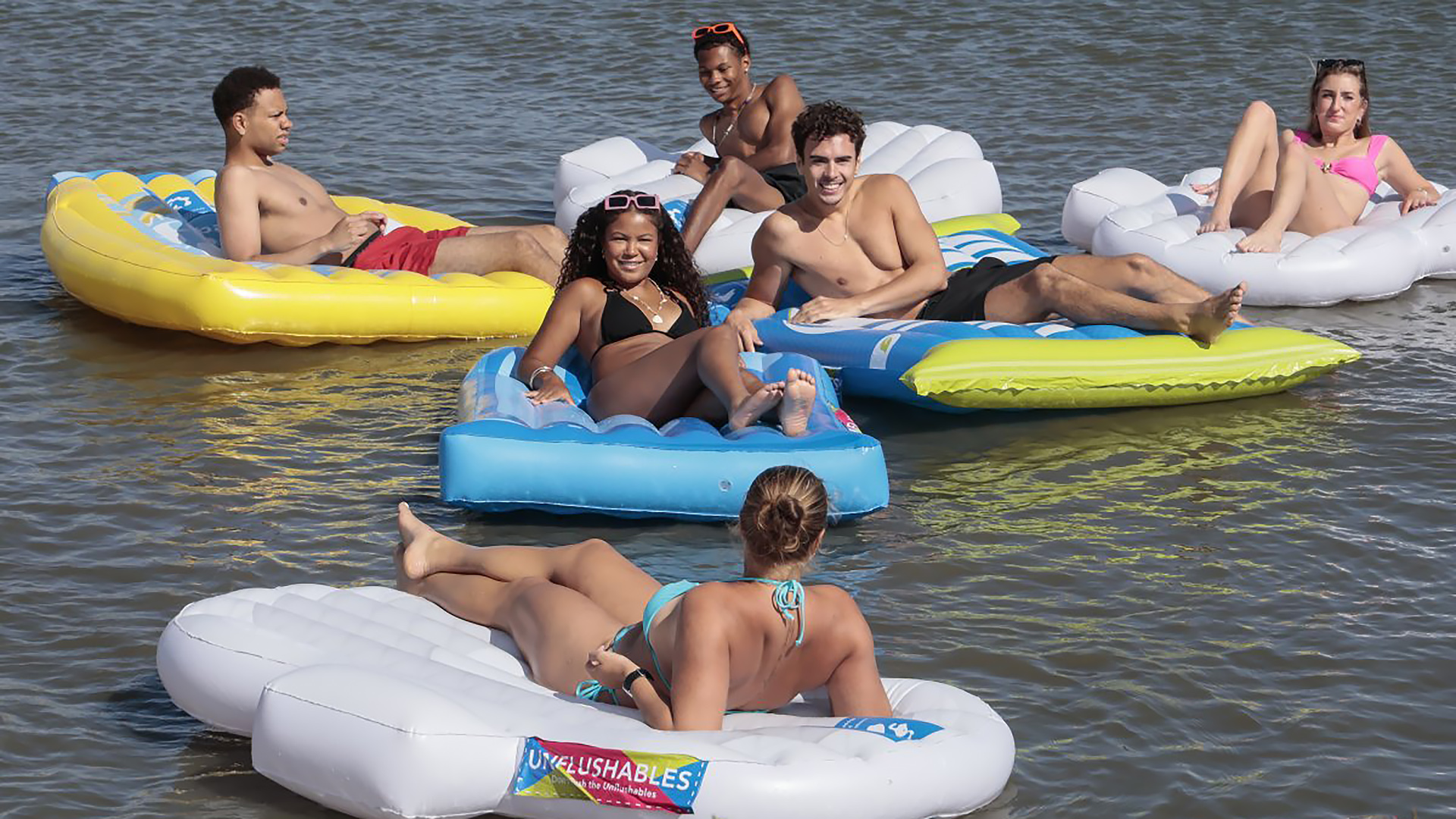 Groep jongeren in zwemkleding dobbert op kleurrijke luchtbedden in ondiep water