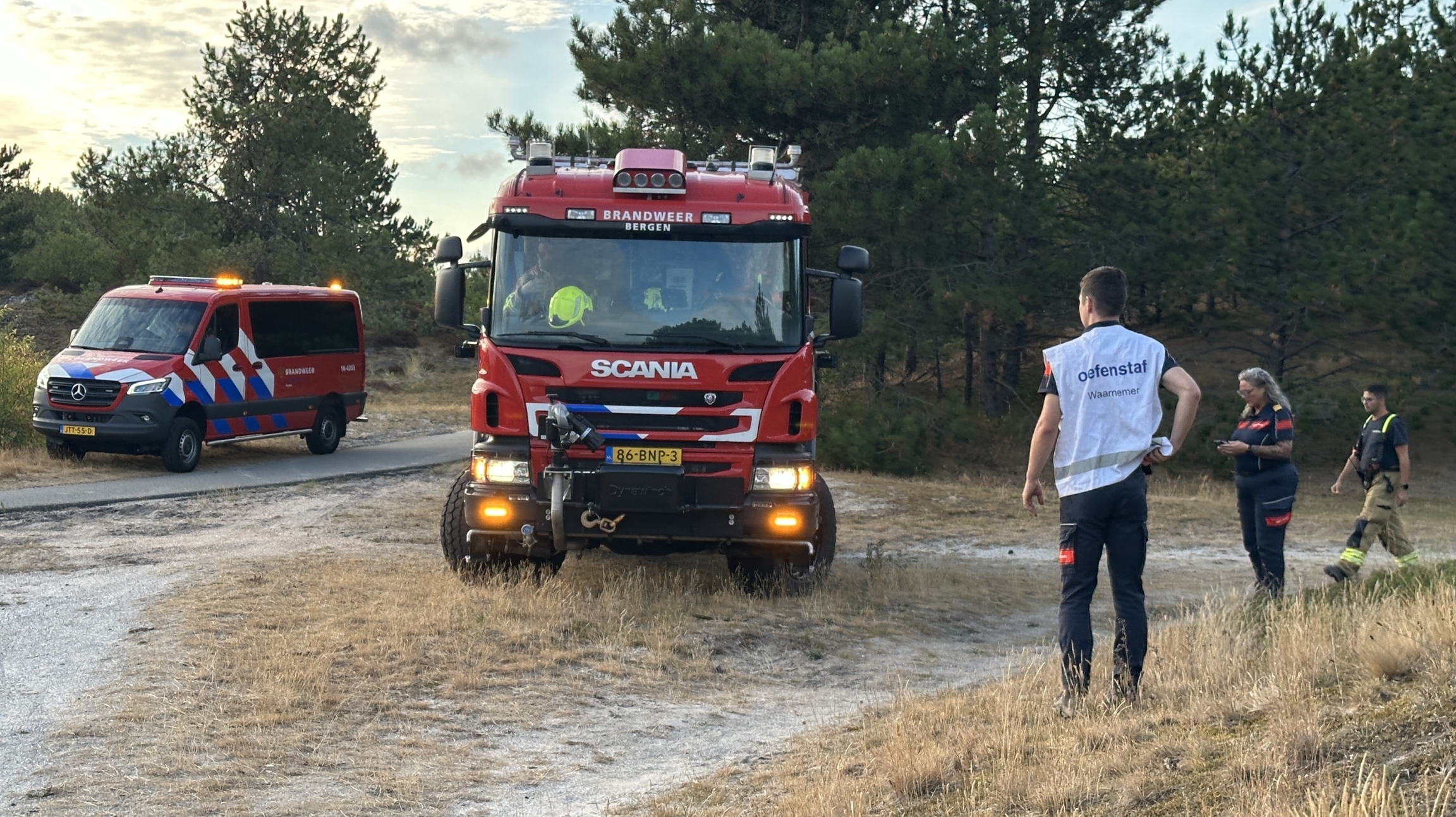 Brandweerwagen en -busje op zandpad in natuurgebied, met hulpverleners die overleggen naast de voertuigen