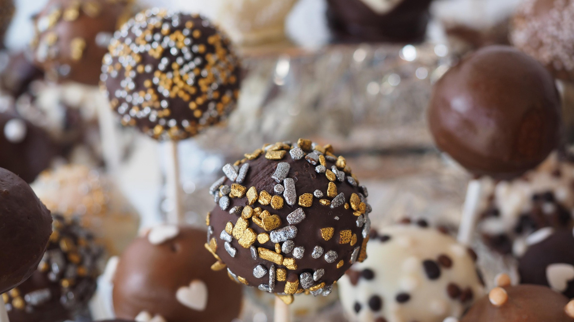 Chocolade cake pops met goud- en zilverkleurige sprinkles, met andere cake pops onscherp op de achtergrond