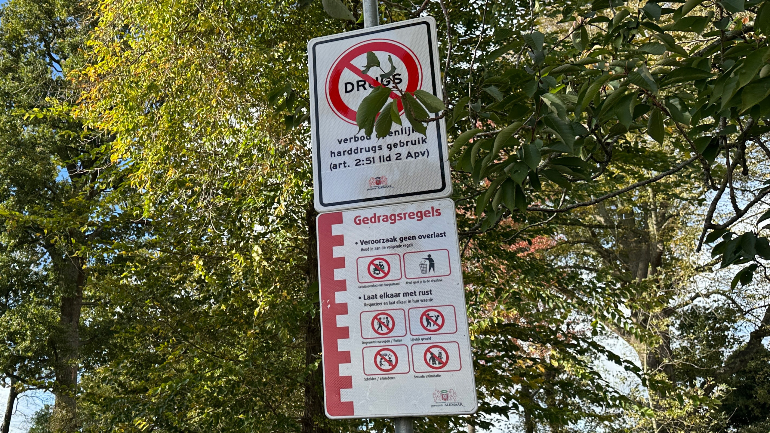 Verkeersbord in park met verboden drugs en gedragsregels tegen overlast, tussen groene bomen