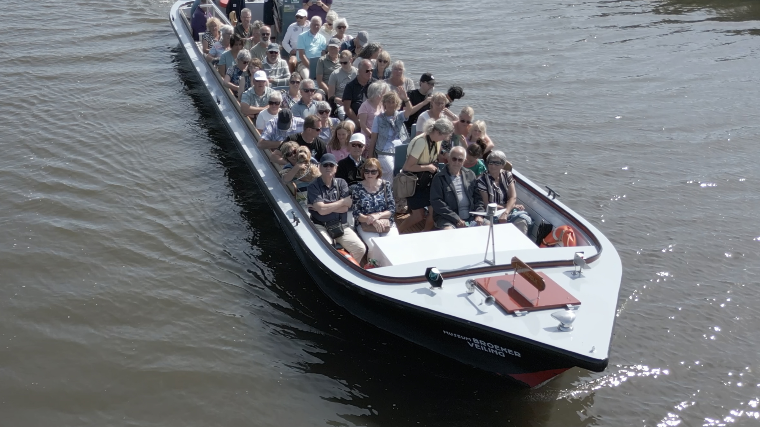 Rondvaartboot vol passagiers vaart over een rivier, gezien schuin van boven