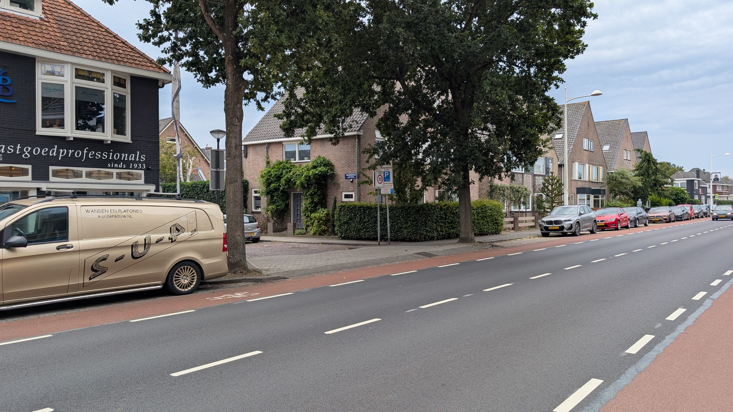 Straat met fietsstrook, geparkeerde auto’s en bestelbus, met bomen en bakstenen huizen langs de weg