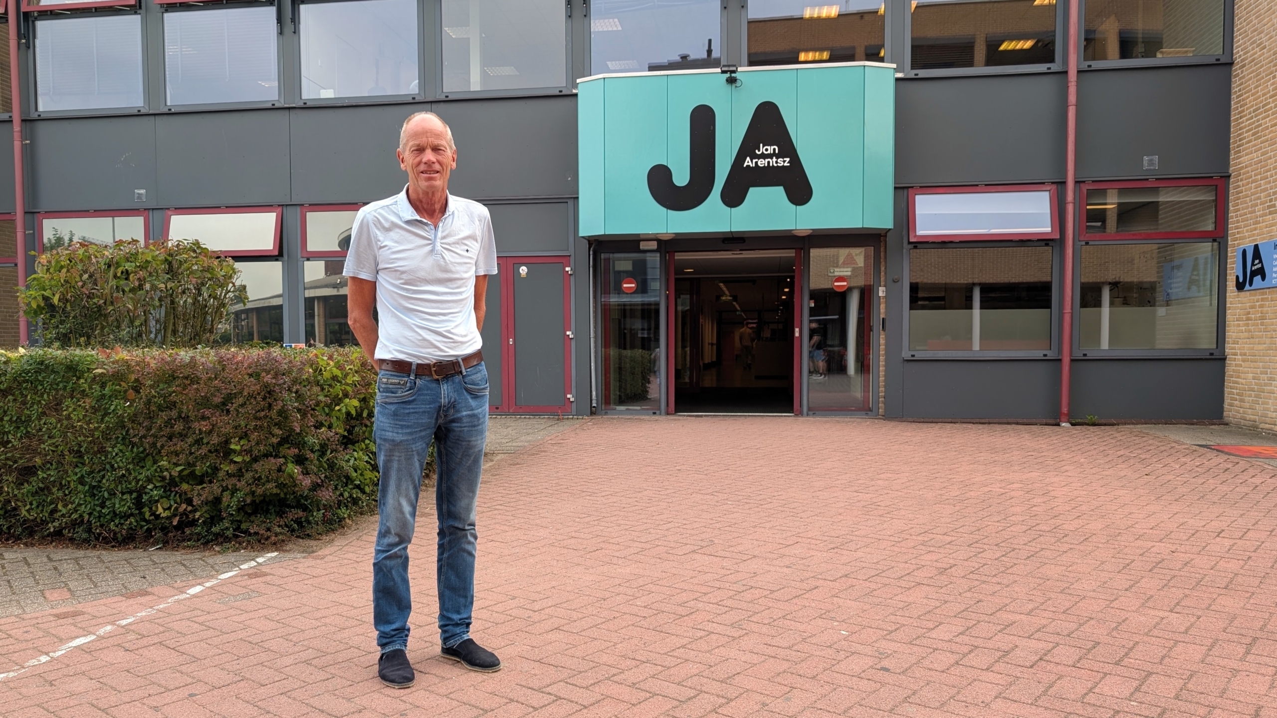 Man staat voor de ingang van een gebouw met turquoise bord met de letters JA en de tekst Jan Arentsz