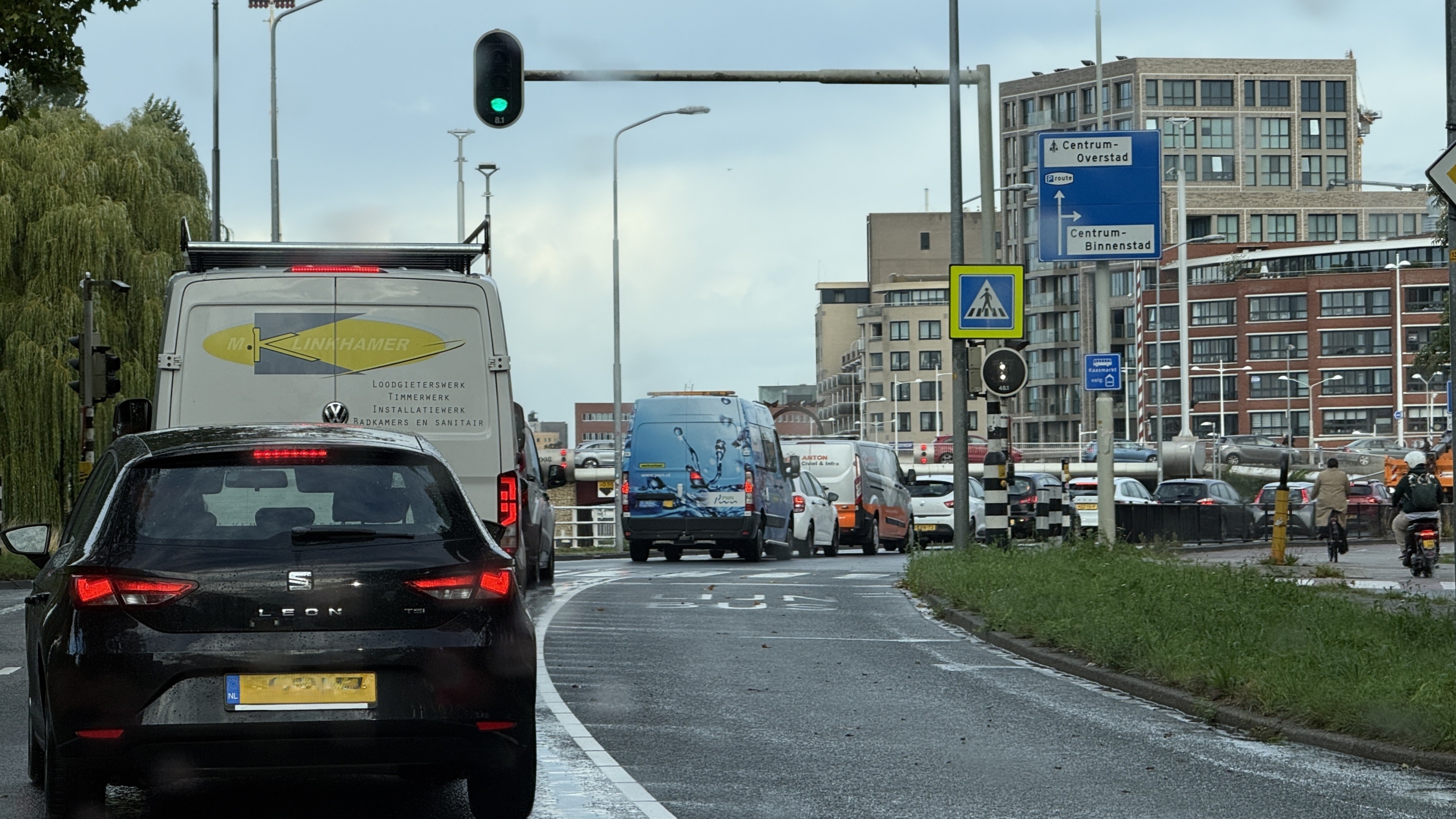 Verkeer bij groen licht met borden naar Centrum-Overstad en Centrum-Binnenstad, met auto’s en bestelbusjes in de stad