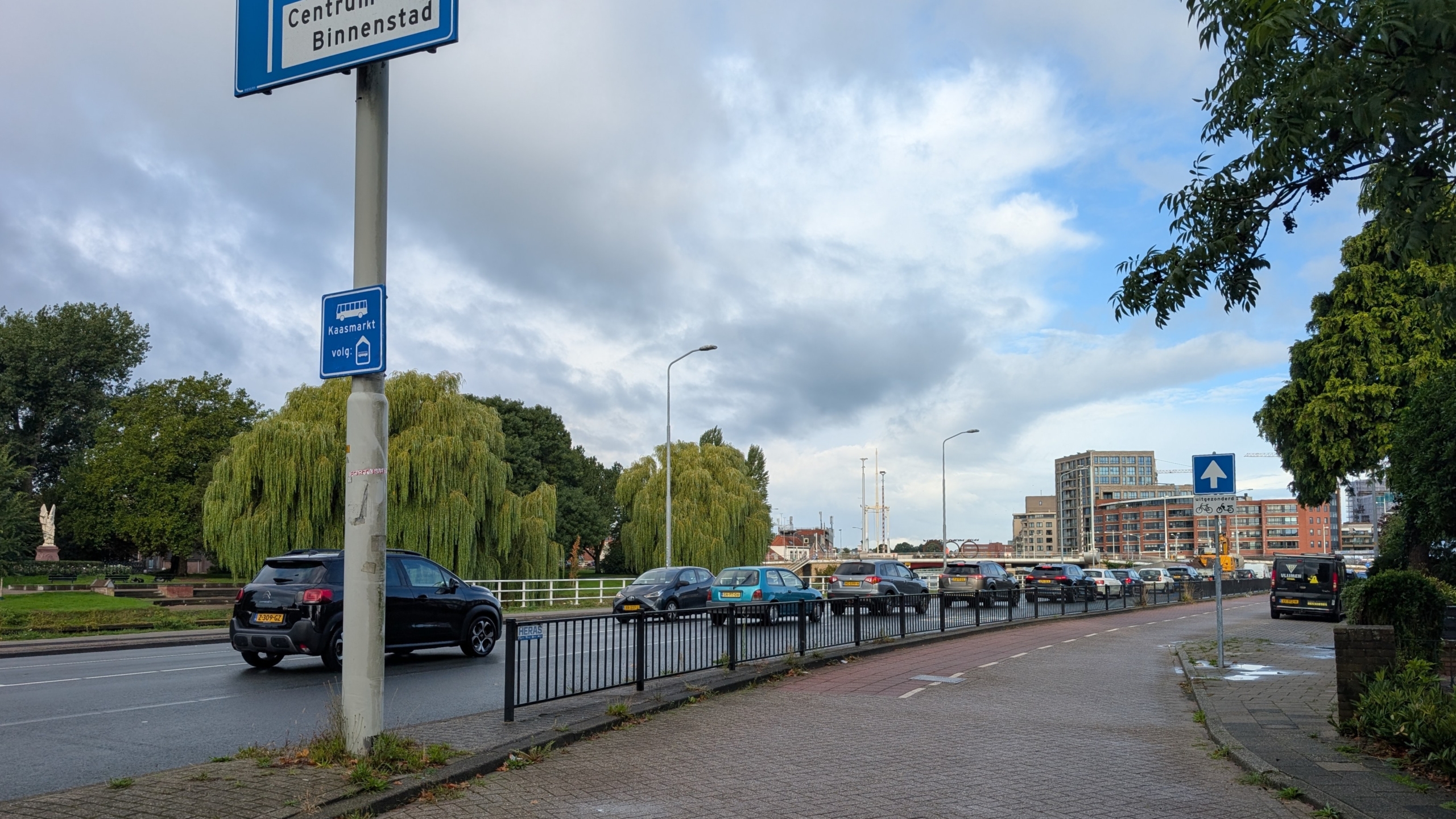 Drukke stadsweg met auto’s, fietspad en borden “Centrum Binnenstad” en “Kaasmarkt volg” onder een bewolkte lucht
