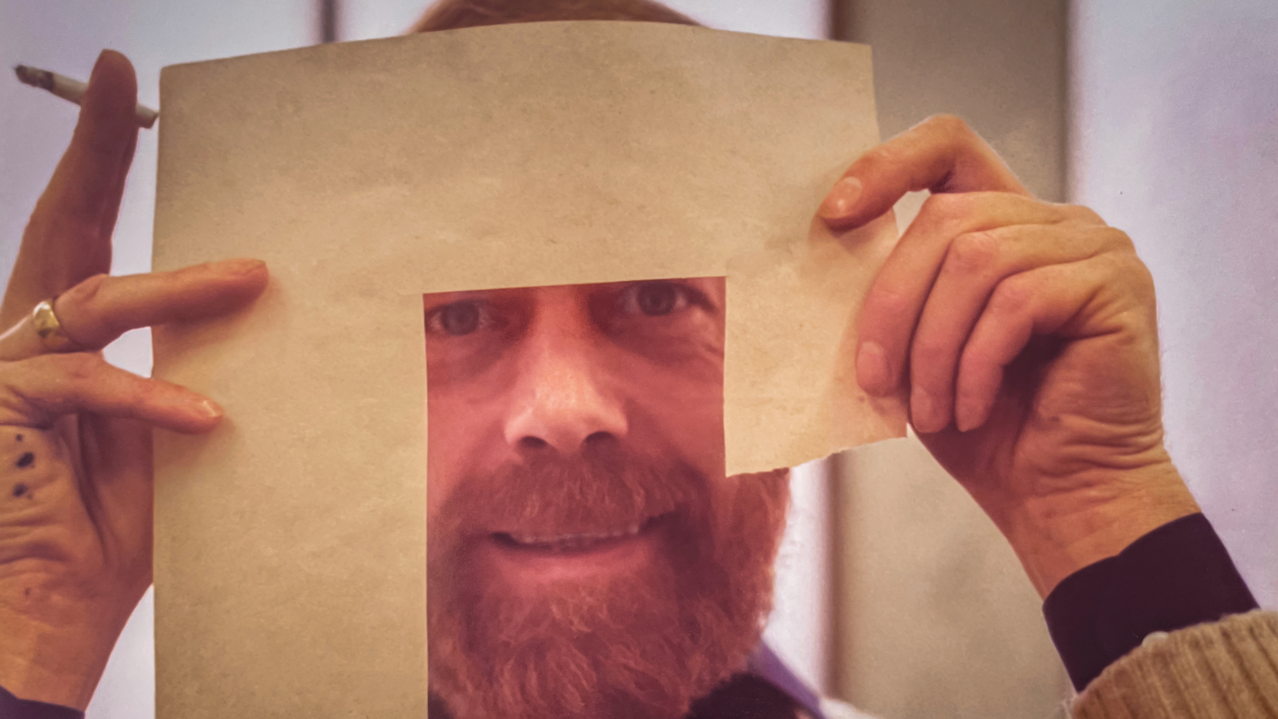 Handen houden een vel papier met een uitsparing, waardoor het gezicht van een man met baard zichtbaar is