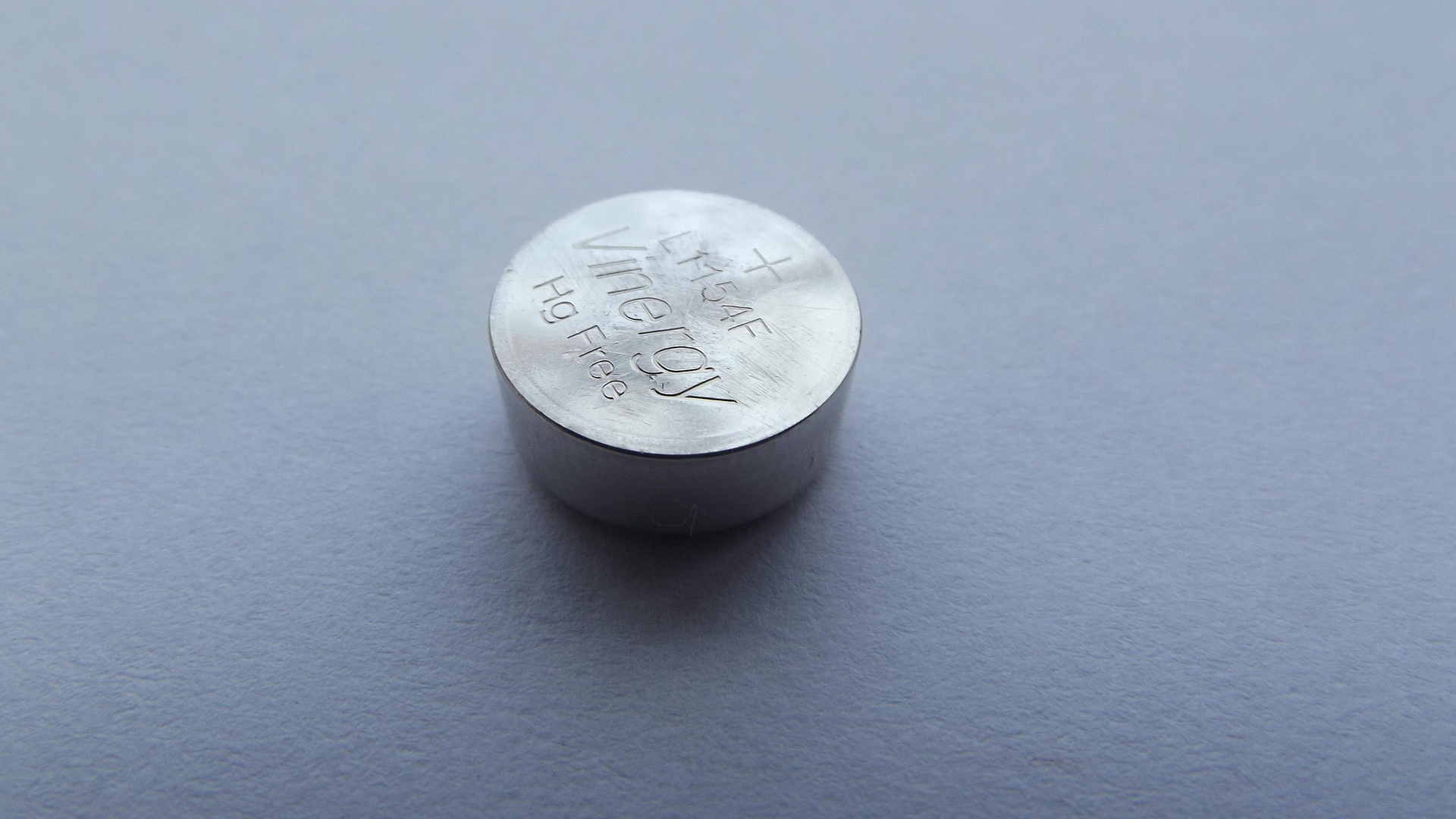Close-up van een zilverkleurige knoopcelbatterij op een grijze ondergrond, met opdruk “Vinnic” en plus-teken