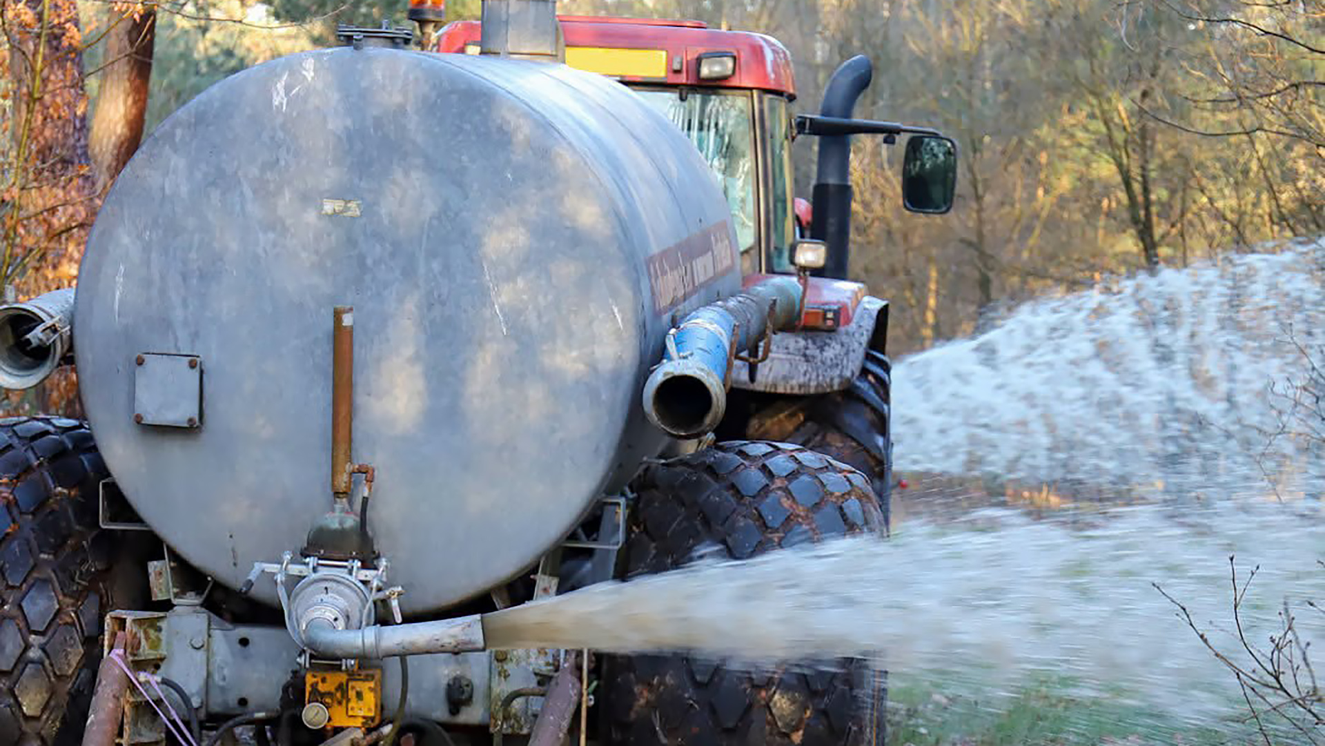 Tractor met watertank die via een slang water sproeit langs een bosrand