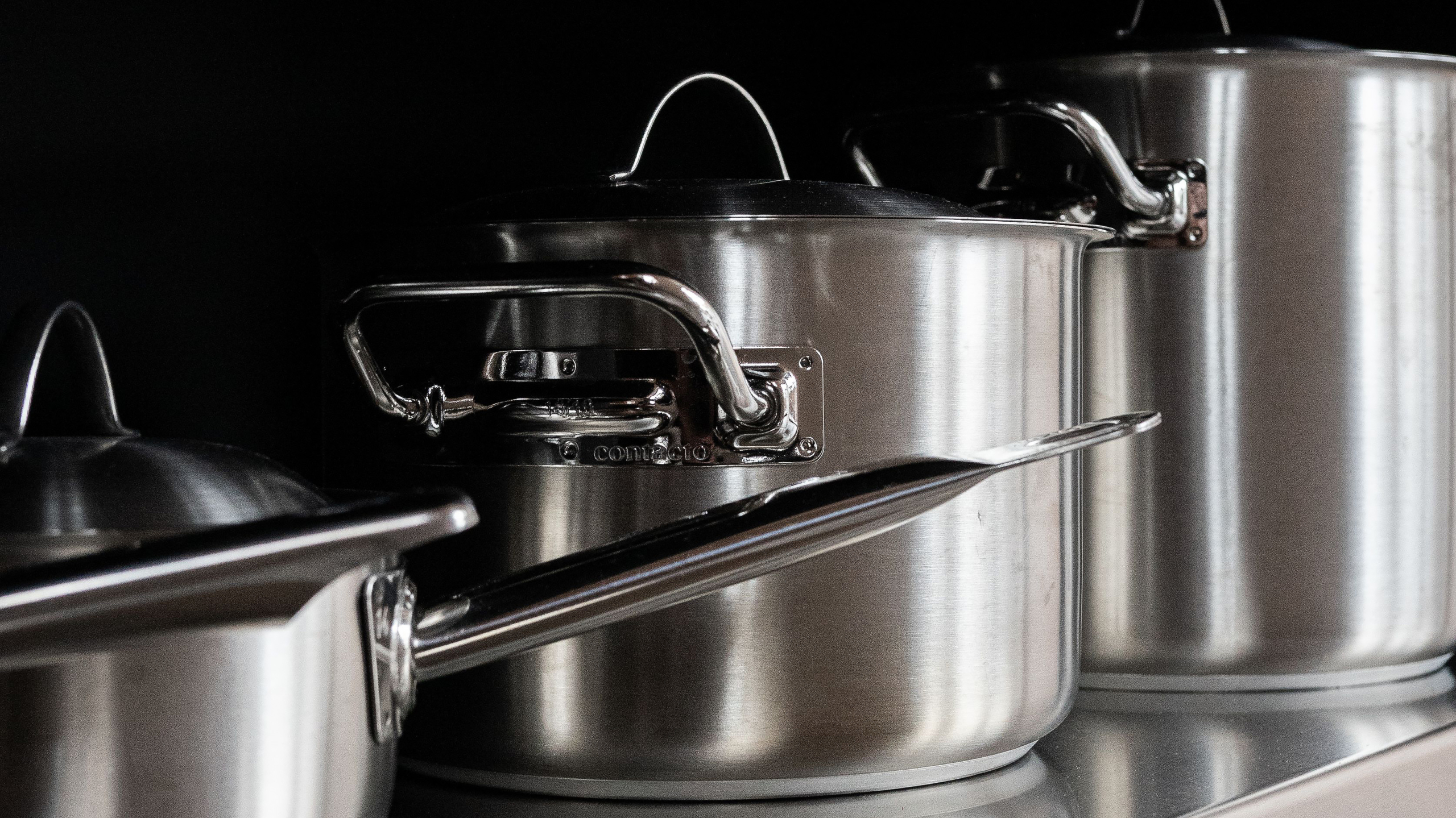 RVS kookpannen met deksels en lange handgrepen, opgesteld naast elkaar in een keuken