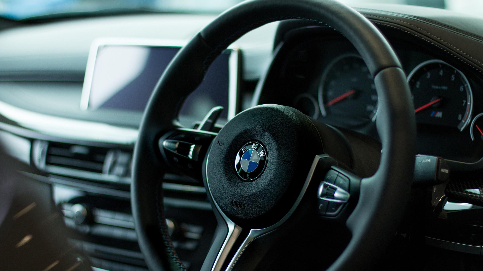 Close-up van het BMW-stuur in een auto-interieur, met dashboardklokken en infotainmentscherm op de achtergrond