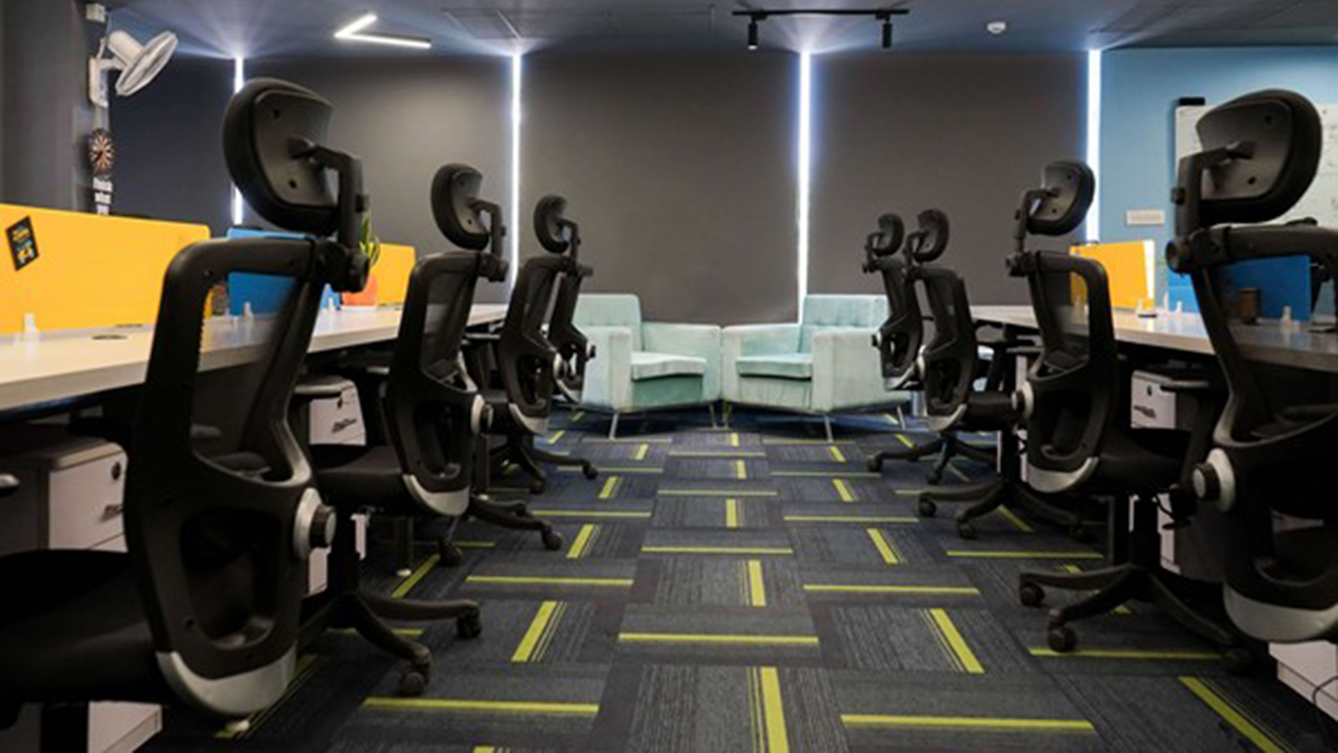 Moderne coworkingruimte met rijen bureaus en zwarte bureaustoelen, met blauwe fauteuils in het midden